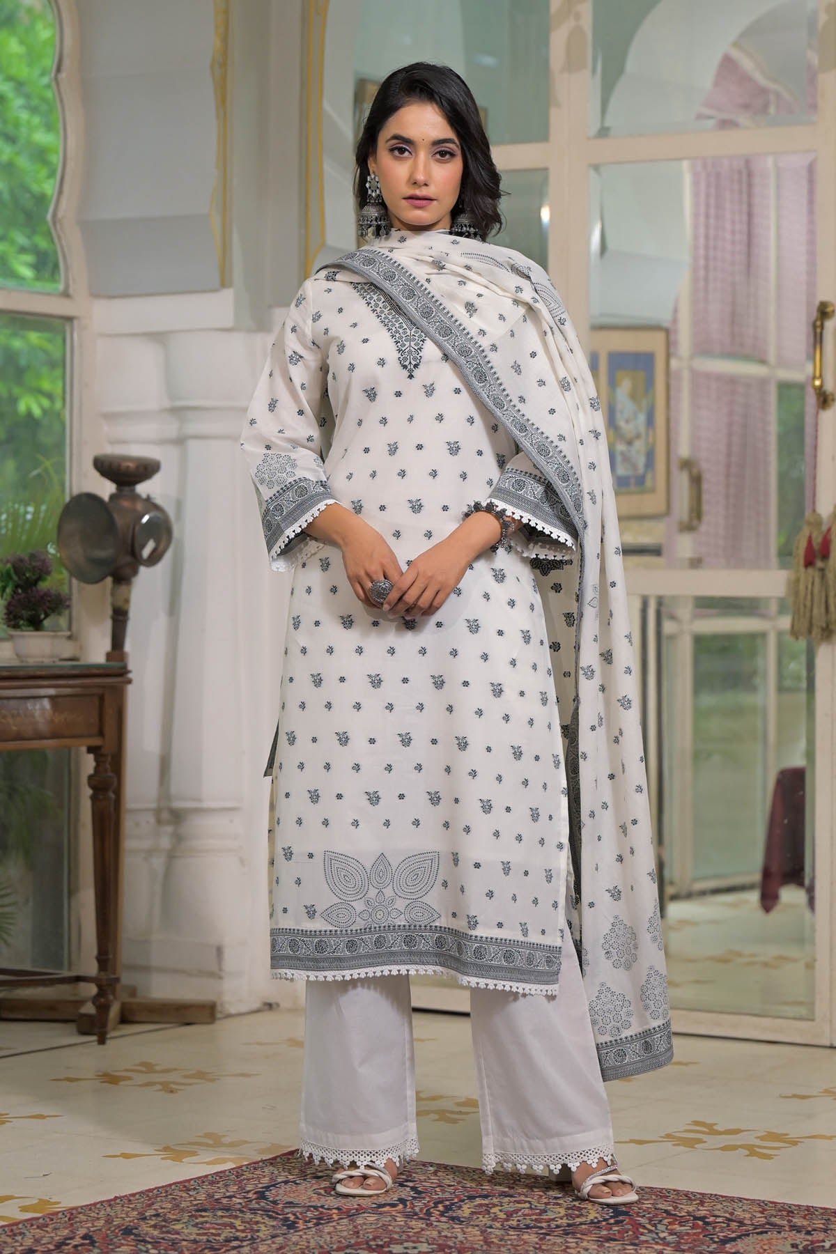 Woman wearing a white traditional outfit with a patterned dupatta in an indoor setting.