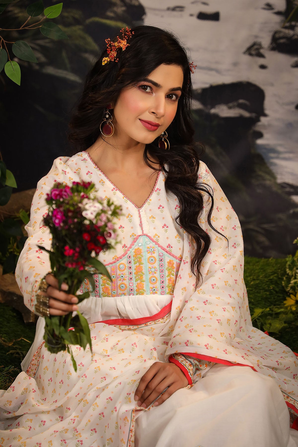 Woman in traditional outfit holding flowers by a water body