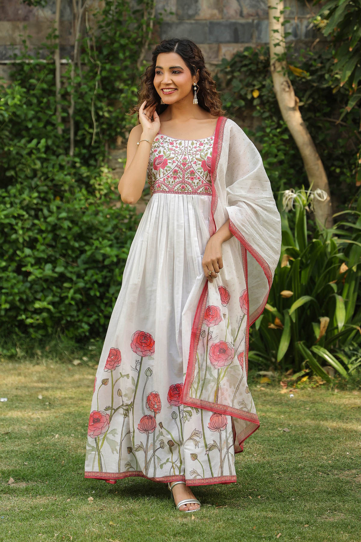 Woman in a white and pink traditional outfit with floral patterns standing outdoors.