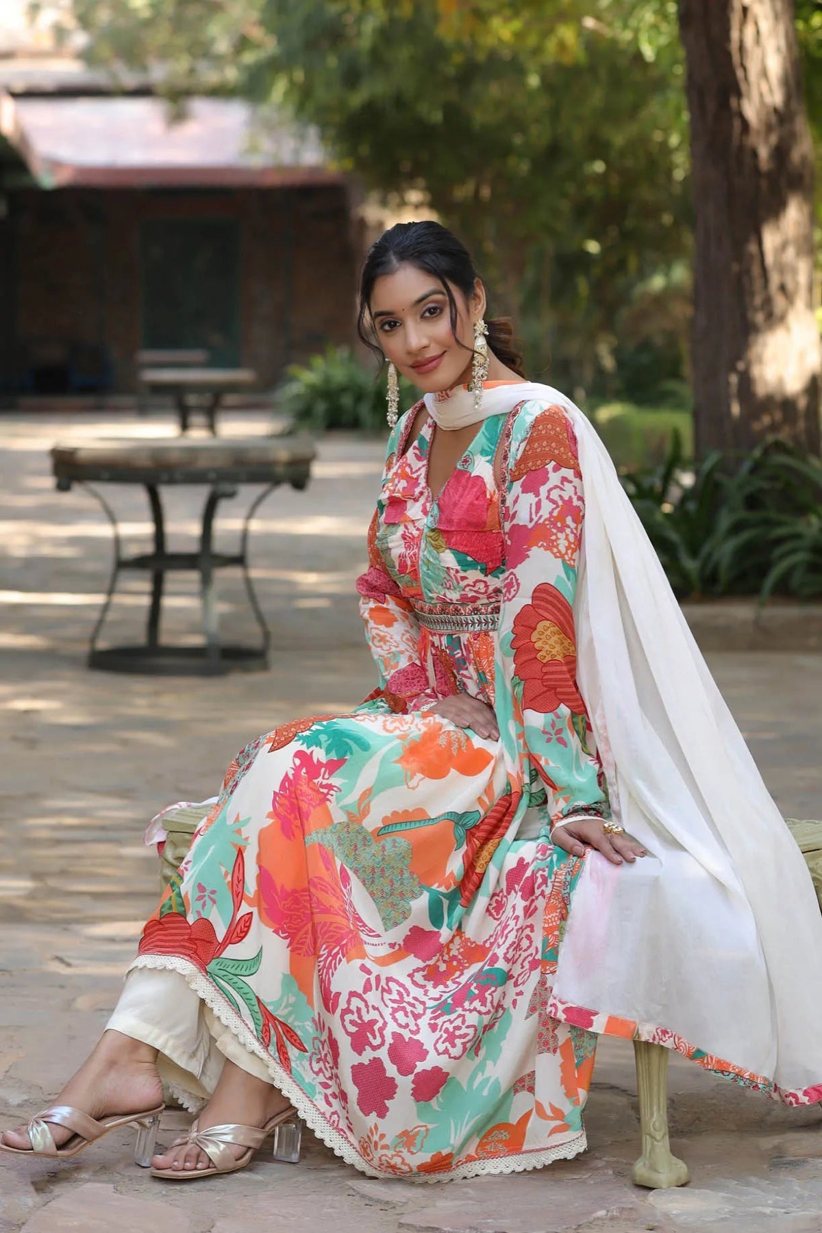 Woman in a colorful floral dress sitting outdoors with trees and benches in the background