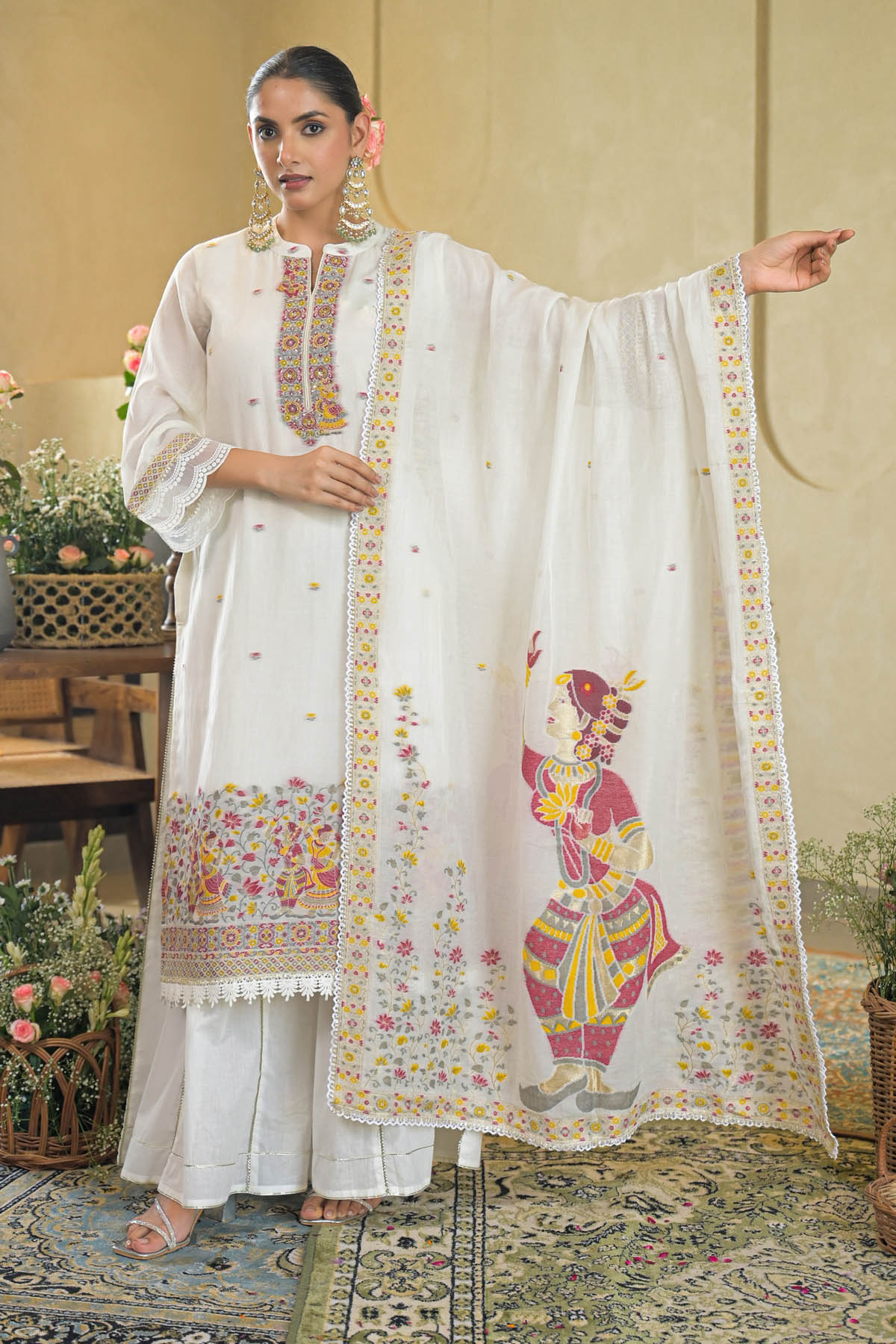 Woman wearing a traditional white embroidered outfit with colorful designs in an indoor setting.