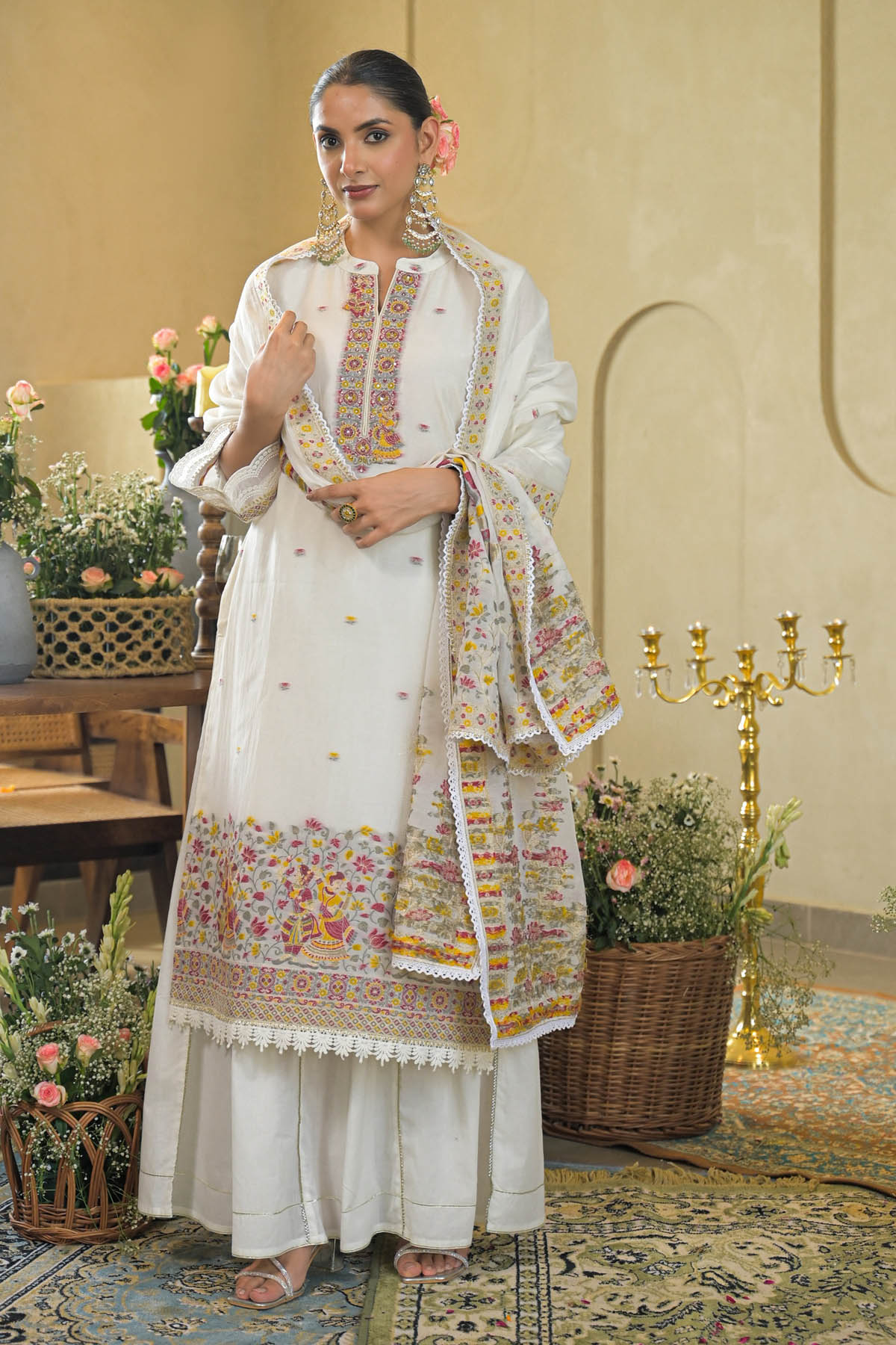 Woman in traditional white outfit with floral patterns in a decorated room.