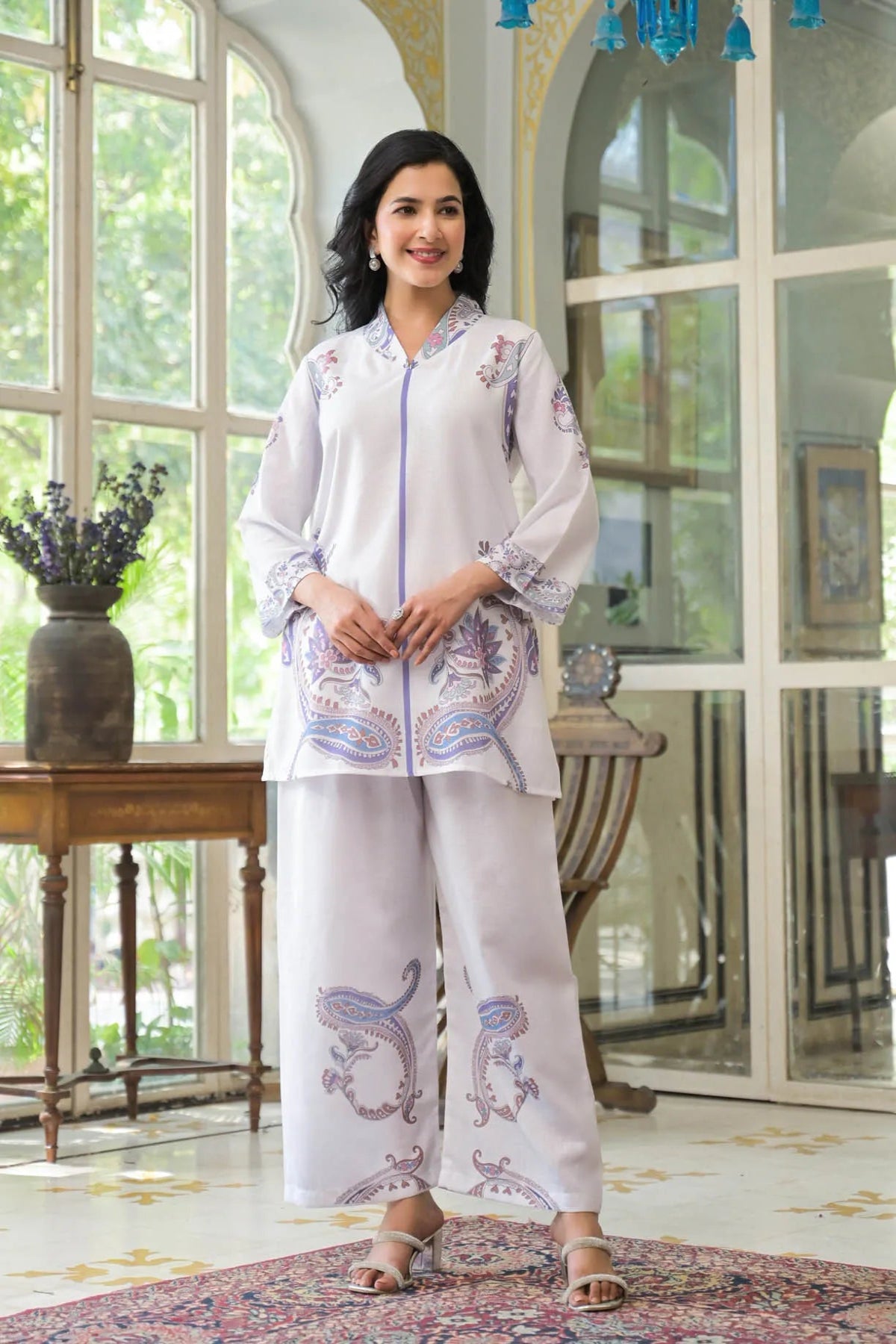 Woman wearing a white embroidered outfit in a room with large windows.