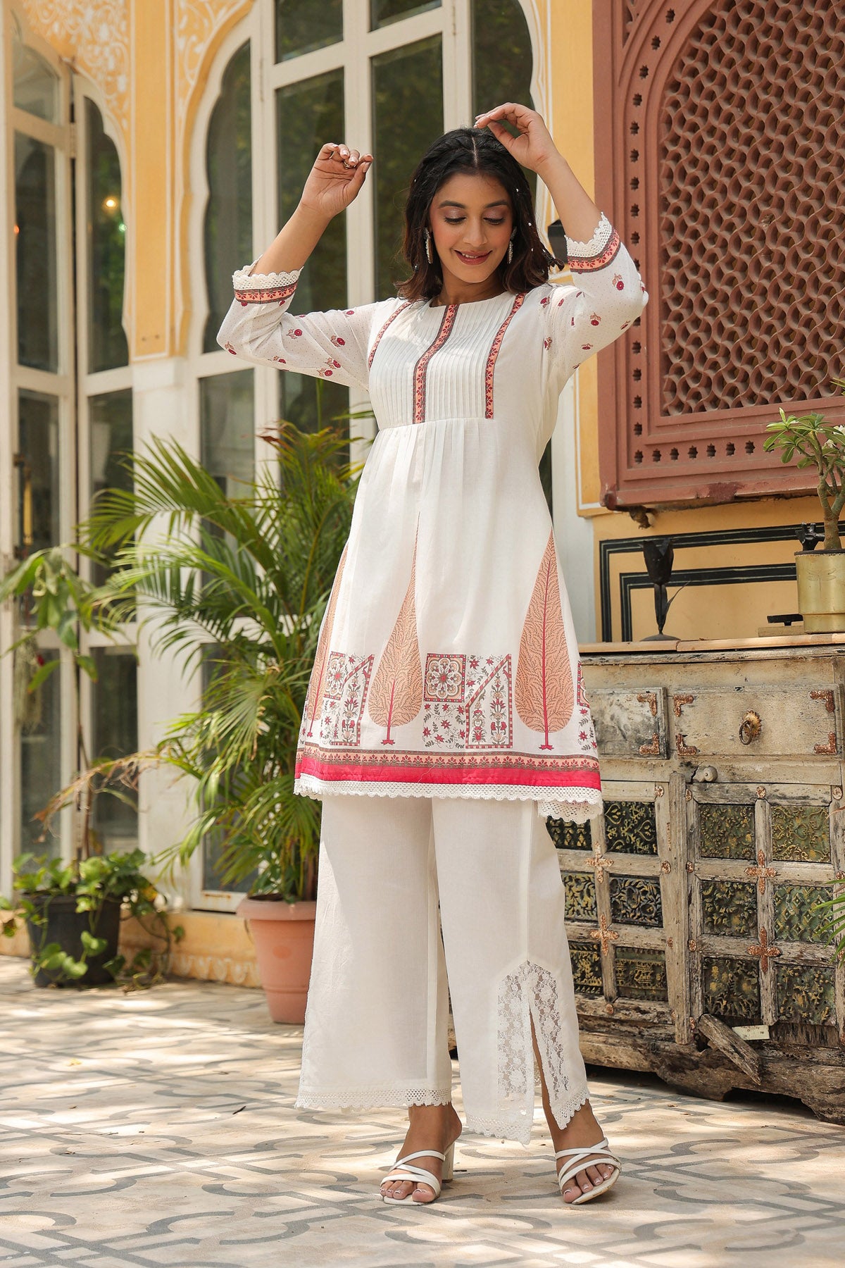 Woman in a white traditional outfit with red and pink embroidery standing in an outdoor setting.