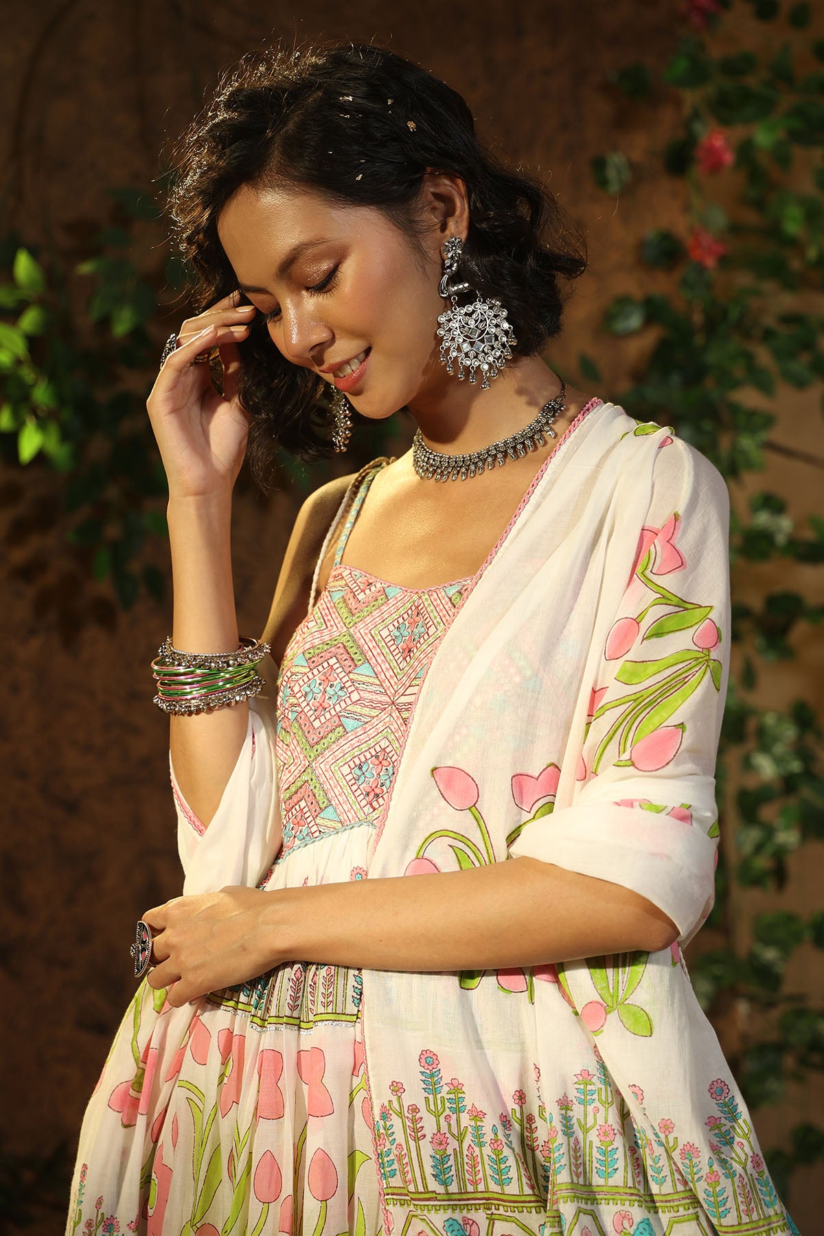 Woman wearing a traditional embroidered saree with floral patterns, standing against a natural background.