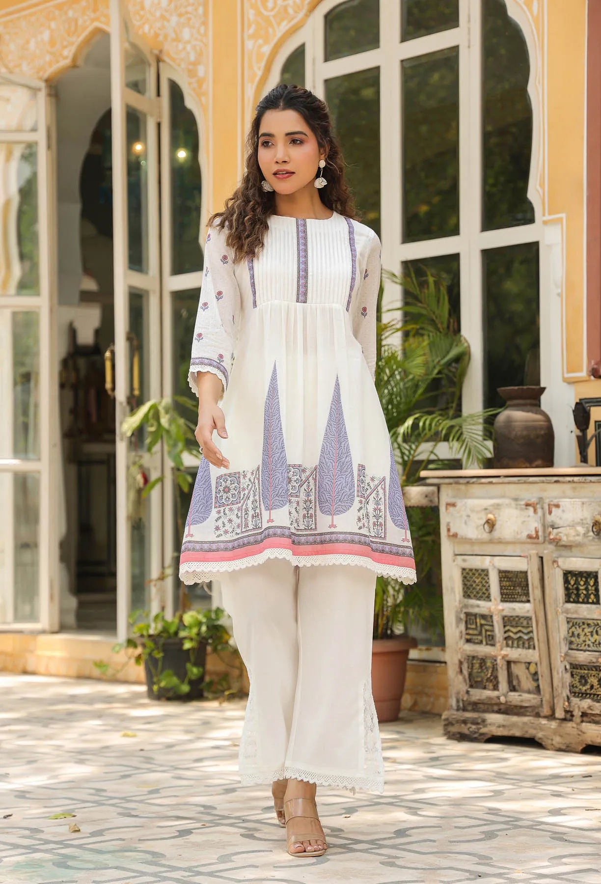 Woman wearing a white and blue embroidered outfit standing in an outdoor setting.