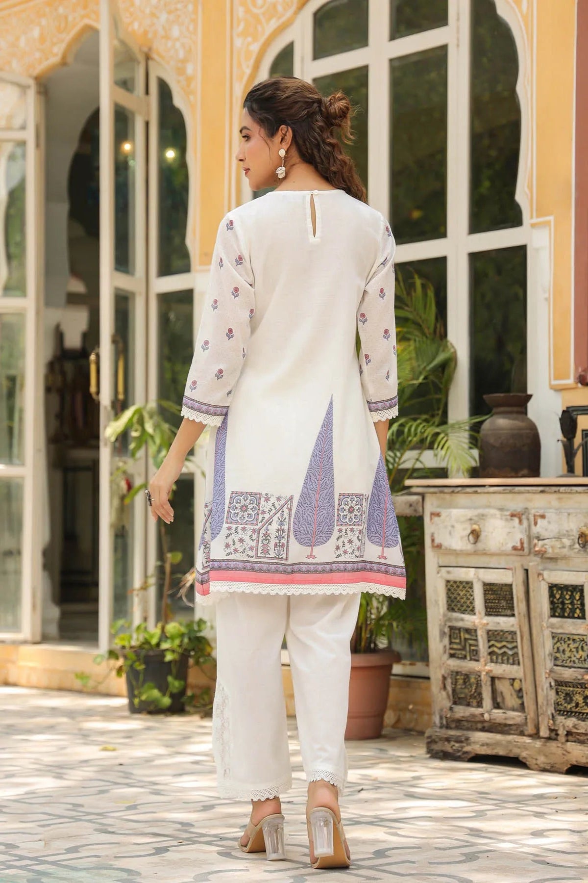 Woman in a white and purple traditional outfit standing in front of a decorative building entrance.