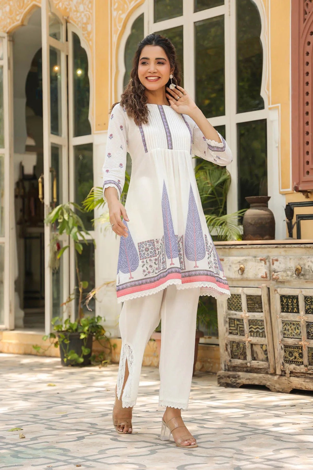 Woman in a white and blue embroidered outfit standing in front of a decorative building.