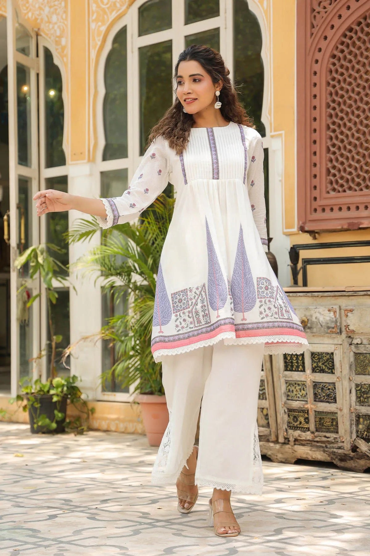 Woman in a white traditional outfit with embroidery standing in front of a decorative building.