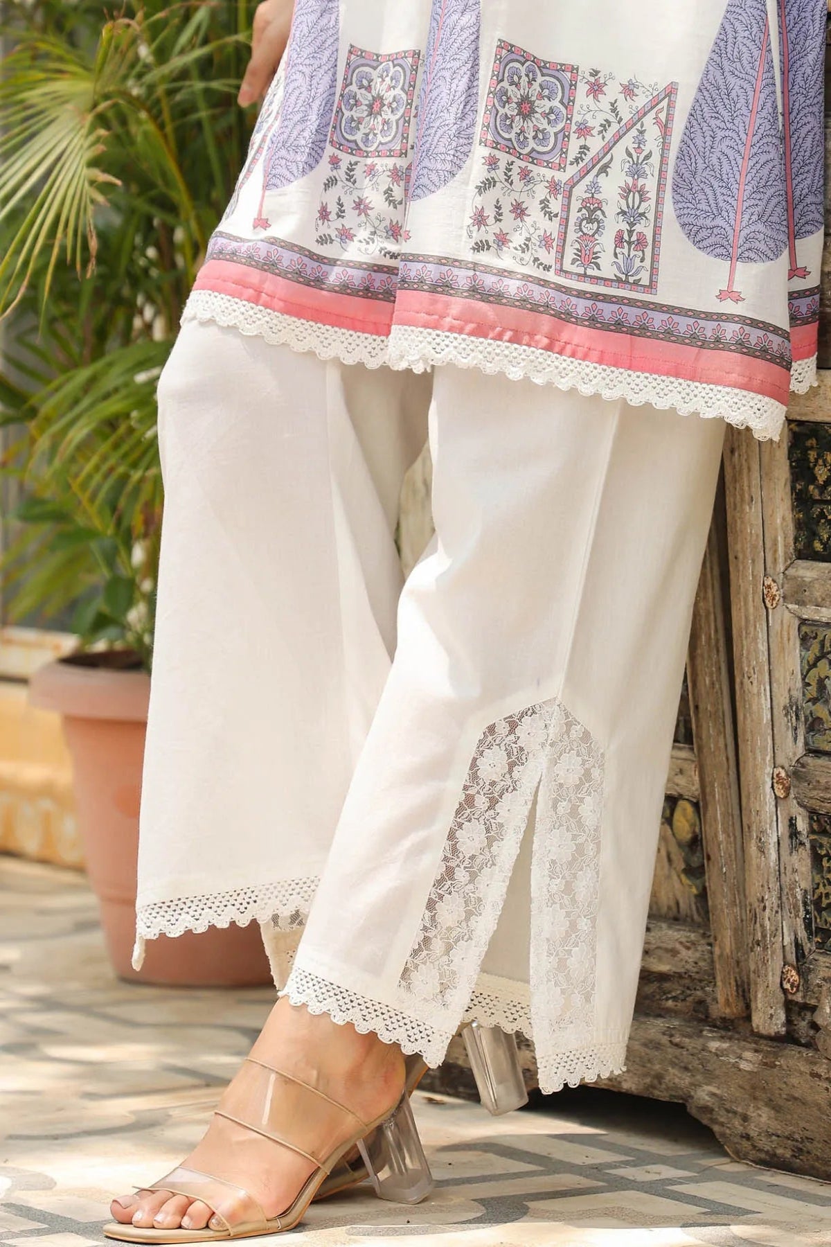 Person wearing a patterned top and white pants with lace details, standing outdoors.