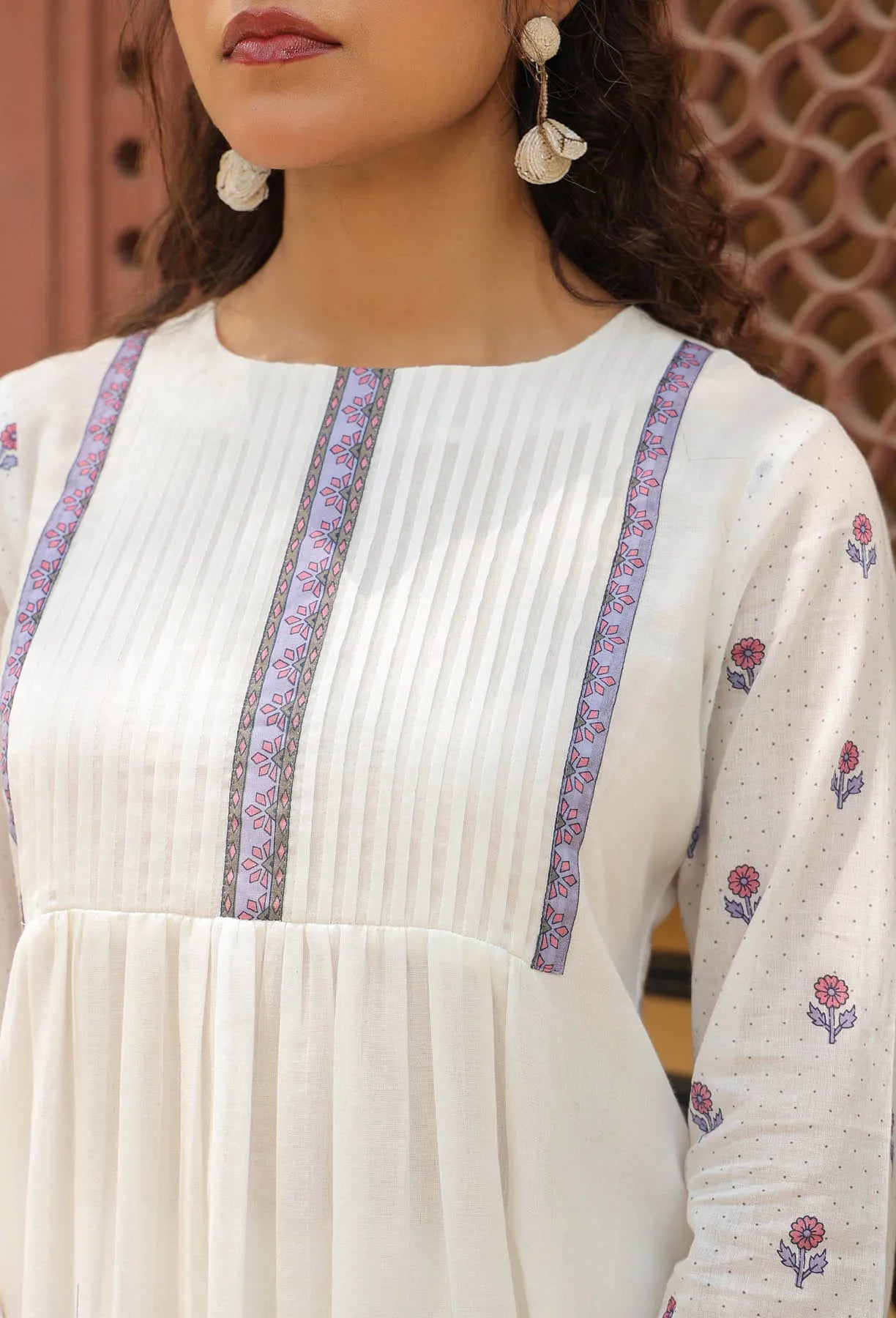 Close-up of a person wearing a white dress with floral patterns and purple accents.