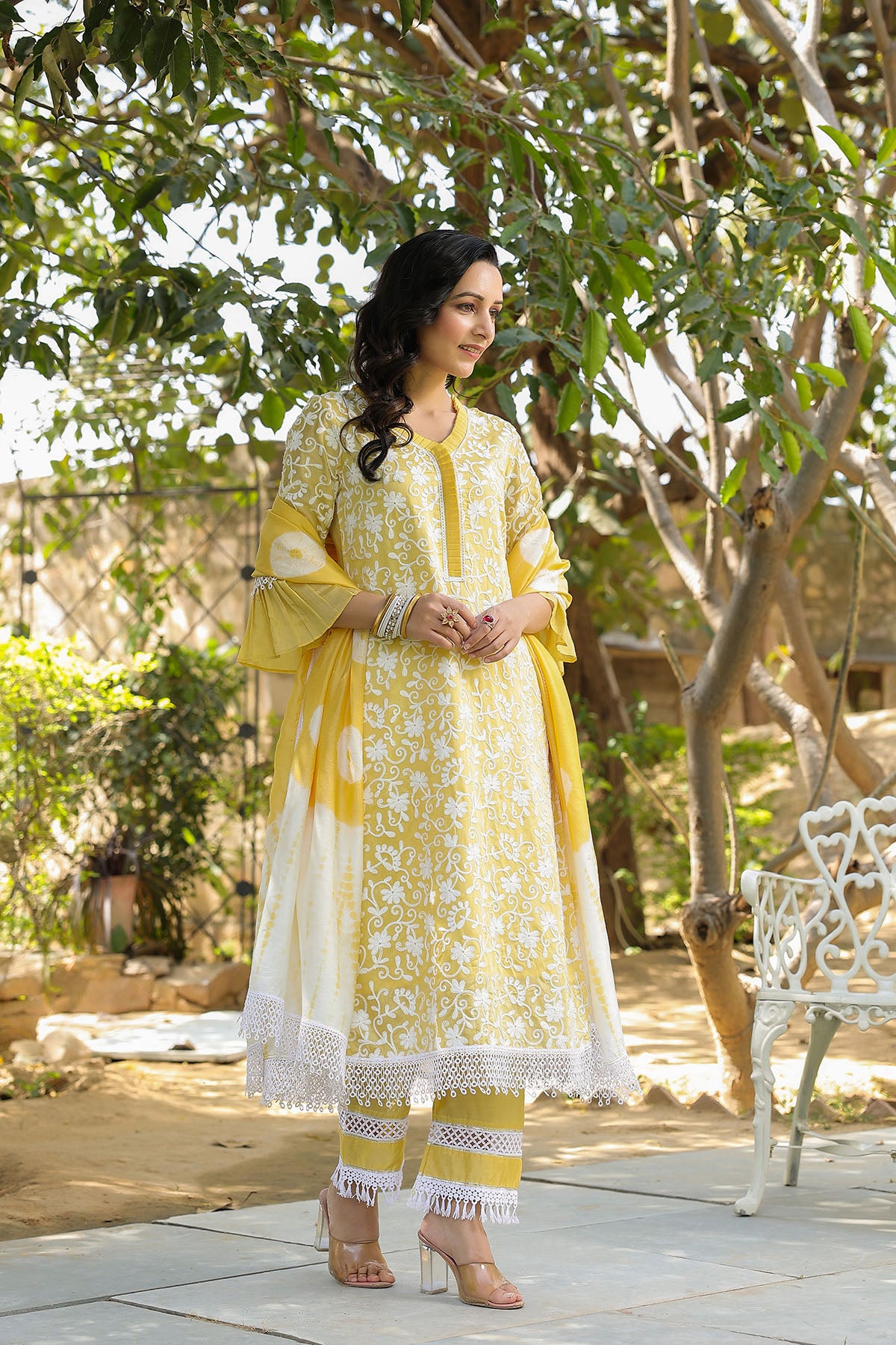Woman in a yellow and white traditional outfit standing outdoors with trees in the background