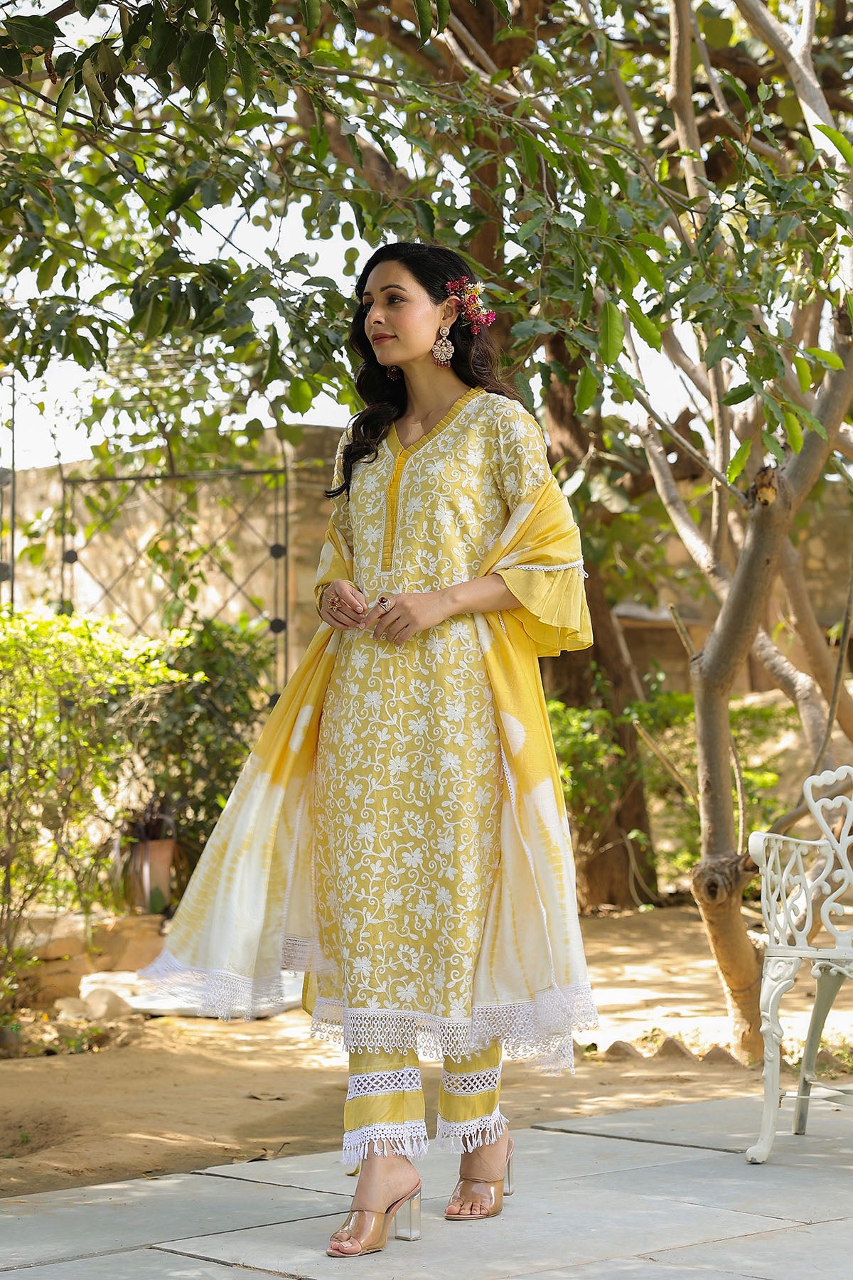 Woman in a yellow and white outfit standing outdoors with greenery in the background