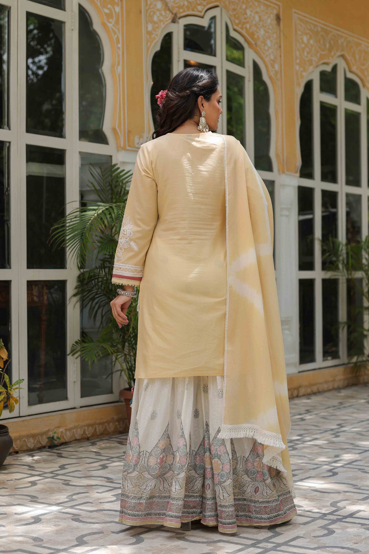 Woman in a traditional outfit standing in front of a building with large windows.