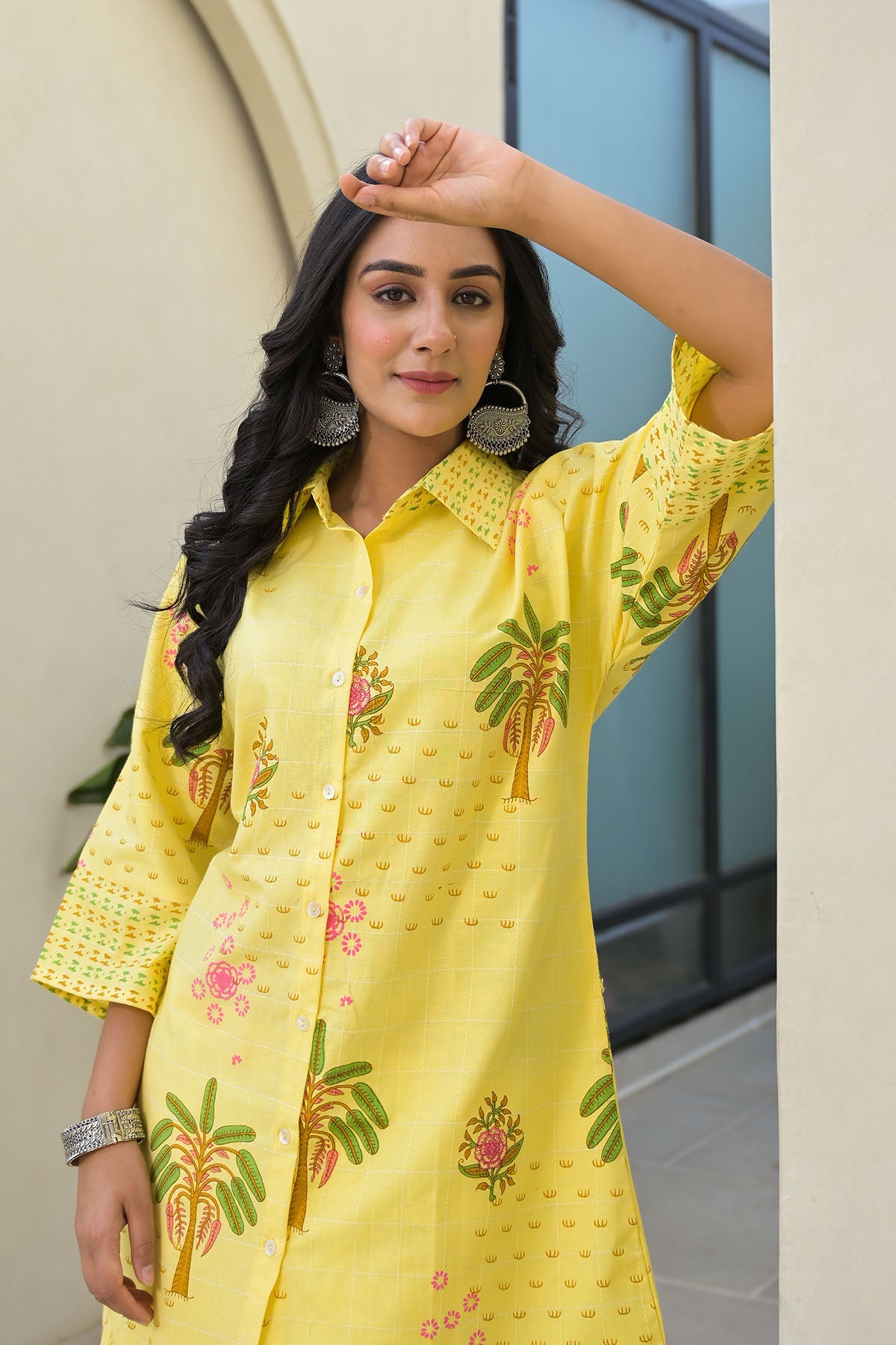 Woman wearing a yellow embroidered kurta with green and pink patterns, standing against a neutral background.