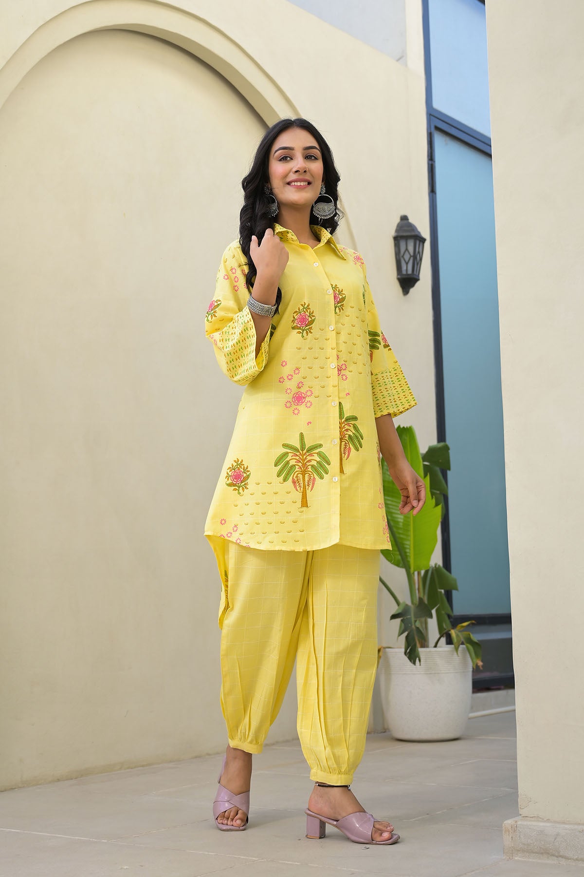 Woman in a yellow traditional outfit with floral patterns standing indoors.