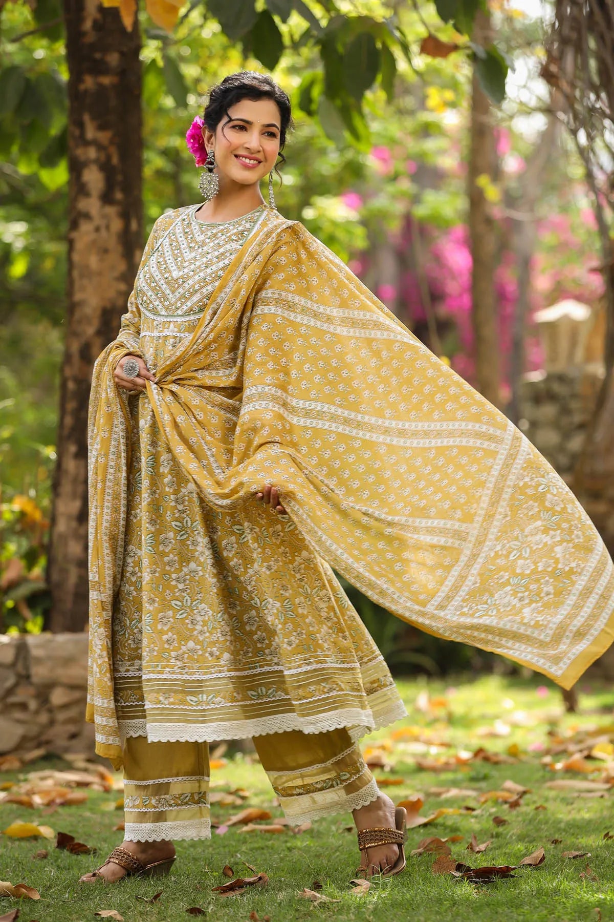 Woman in a yellow traditional outfit standing outdoors with greenery in the background