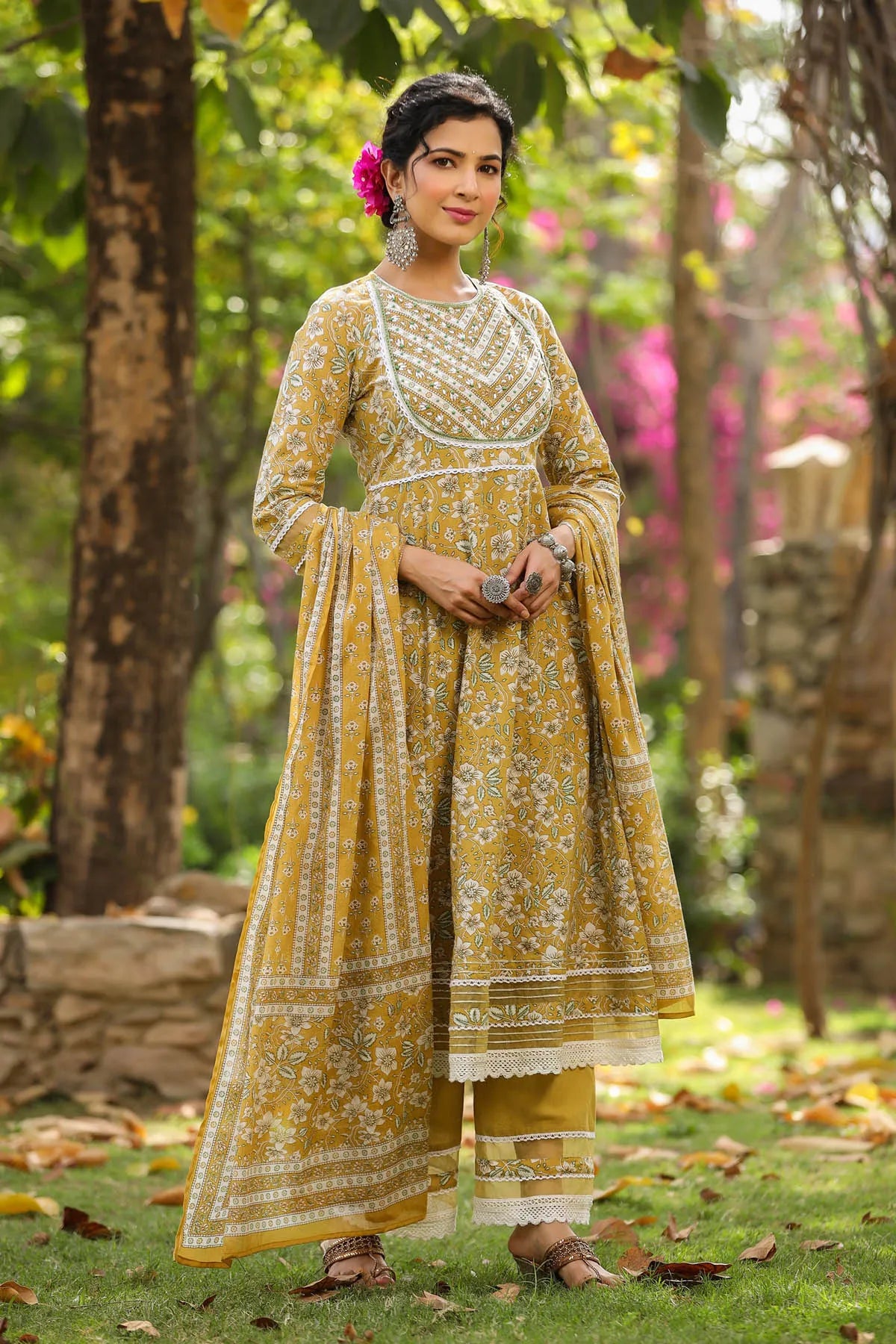 Woman in a yellow traditional outfit with white patterns standing in a garden.