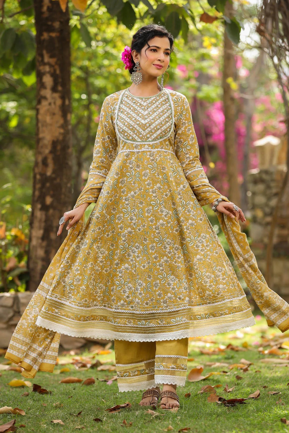 Woman in a yellow and white traditional outfit standing outdoors with greenery in the background