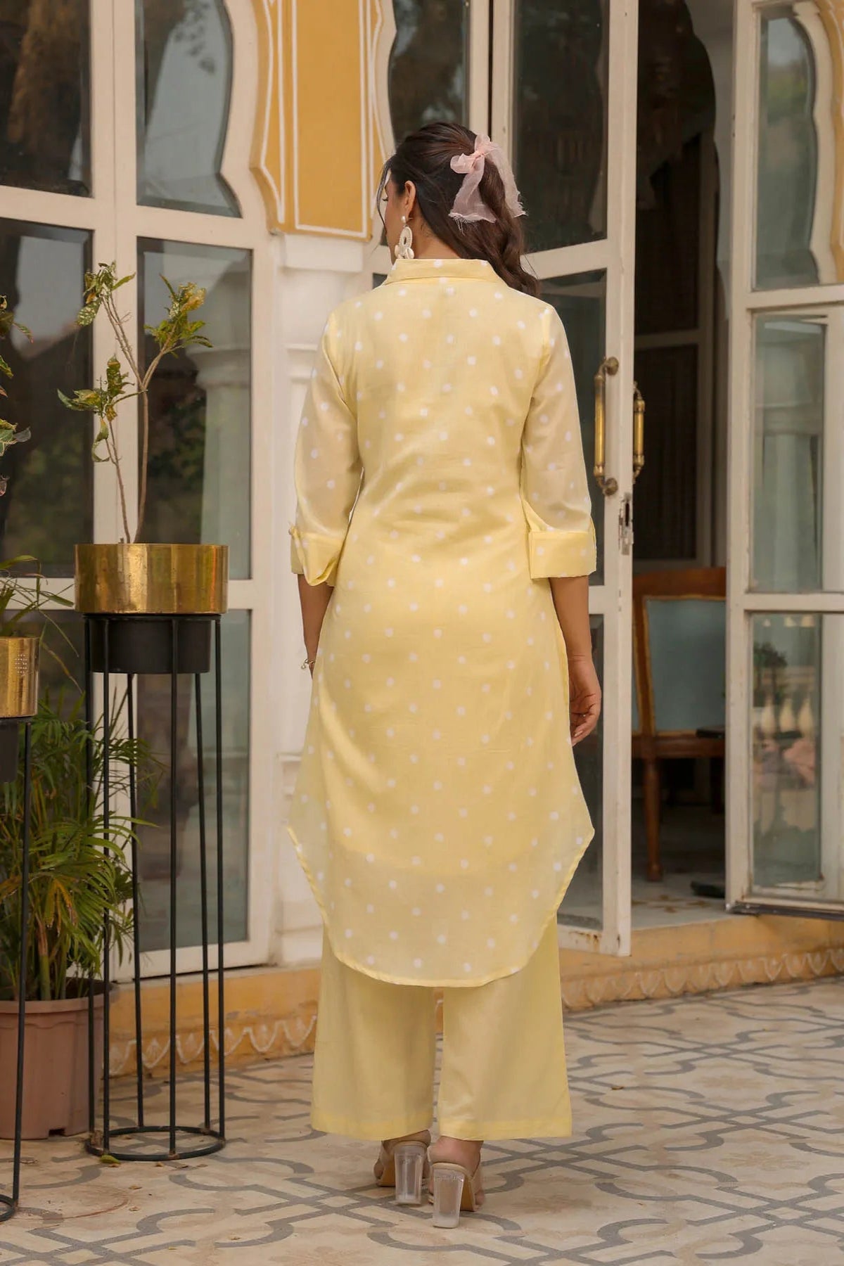 Woman in a yellow traditional outfit standing in front of a glass door.