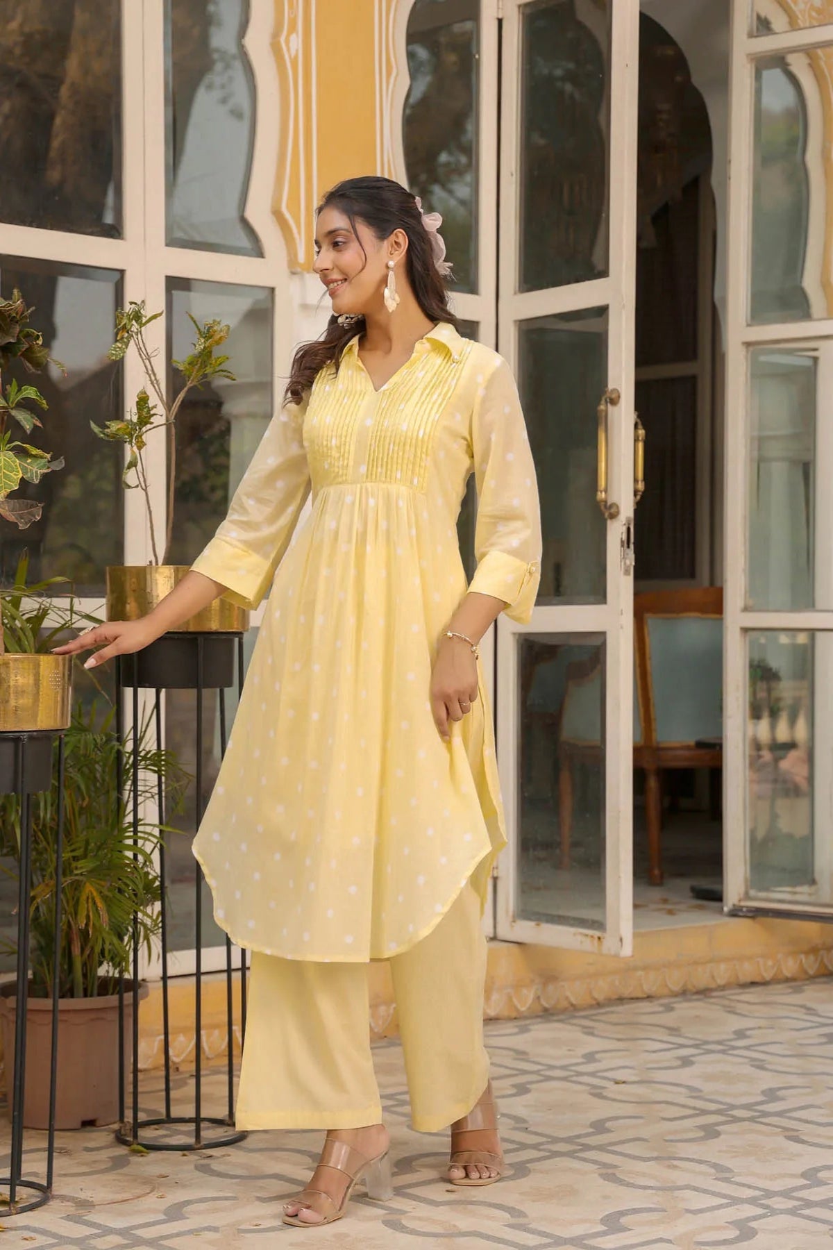 Woman in a yellow outfit standing outdoors near a building entrance.