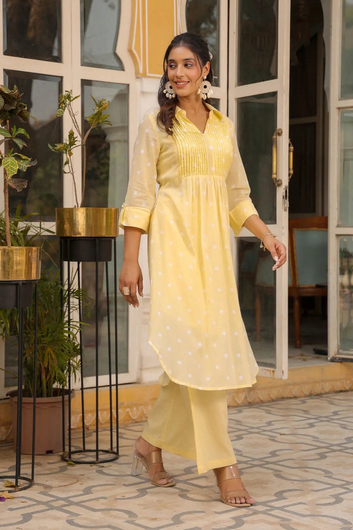 Woman in a yellow outfit standing in front of a glass door with plants around.