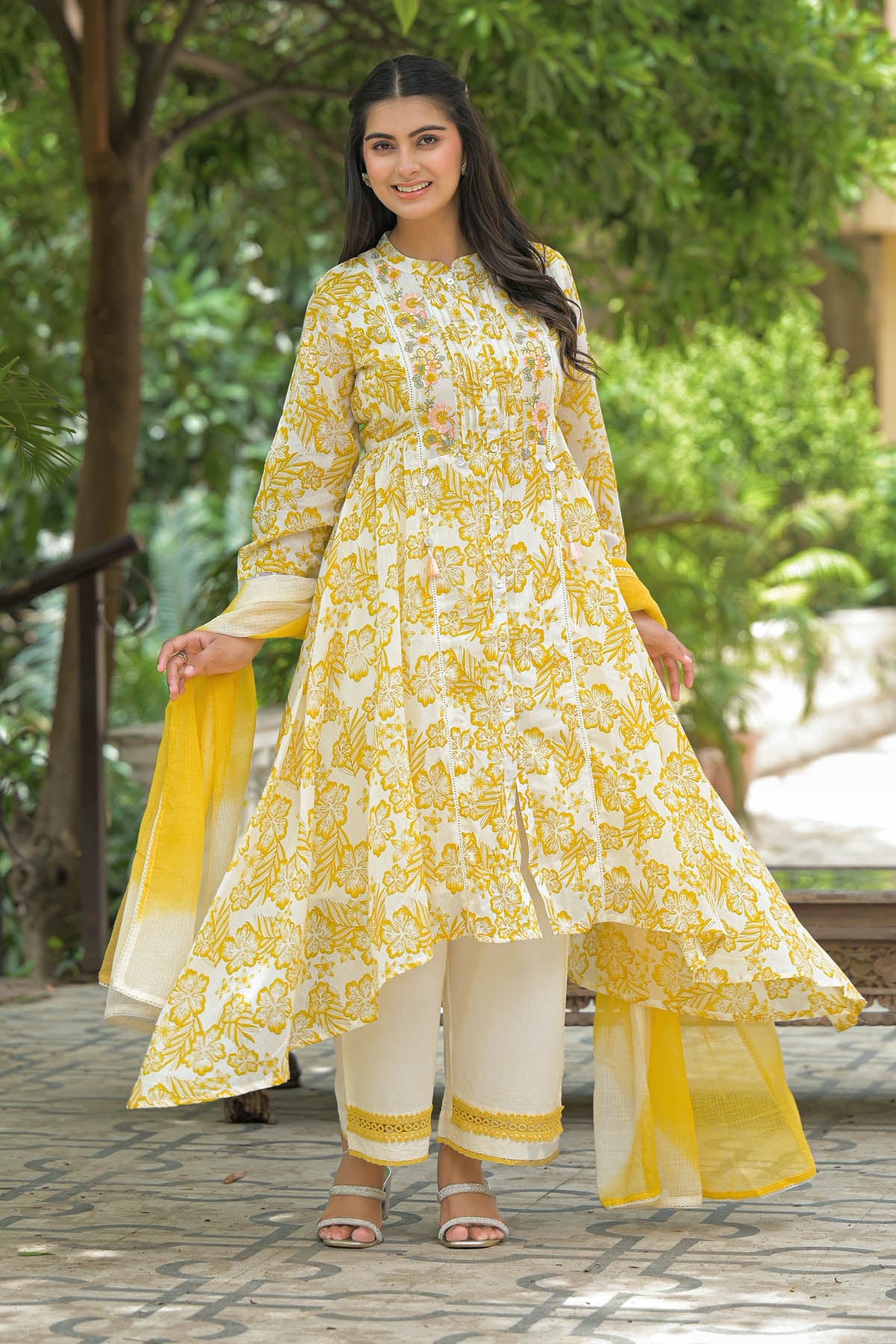 Woman wearing a yellow and white floral outfit with a green outdoor background