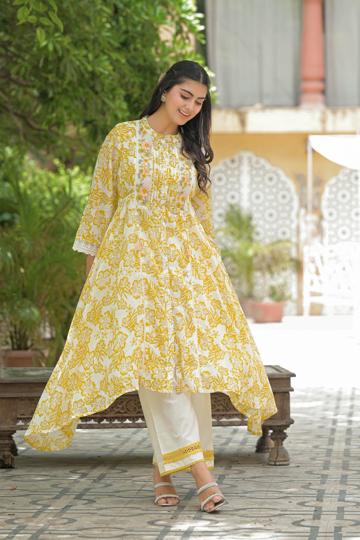 Woman wearing a yellow floral dress standing outdoors with greenery in the background