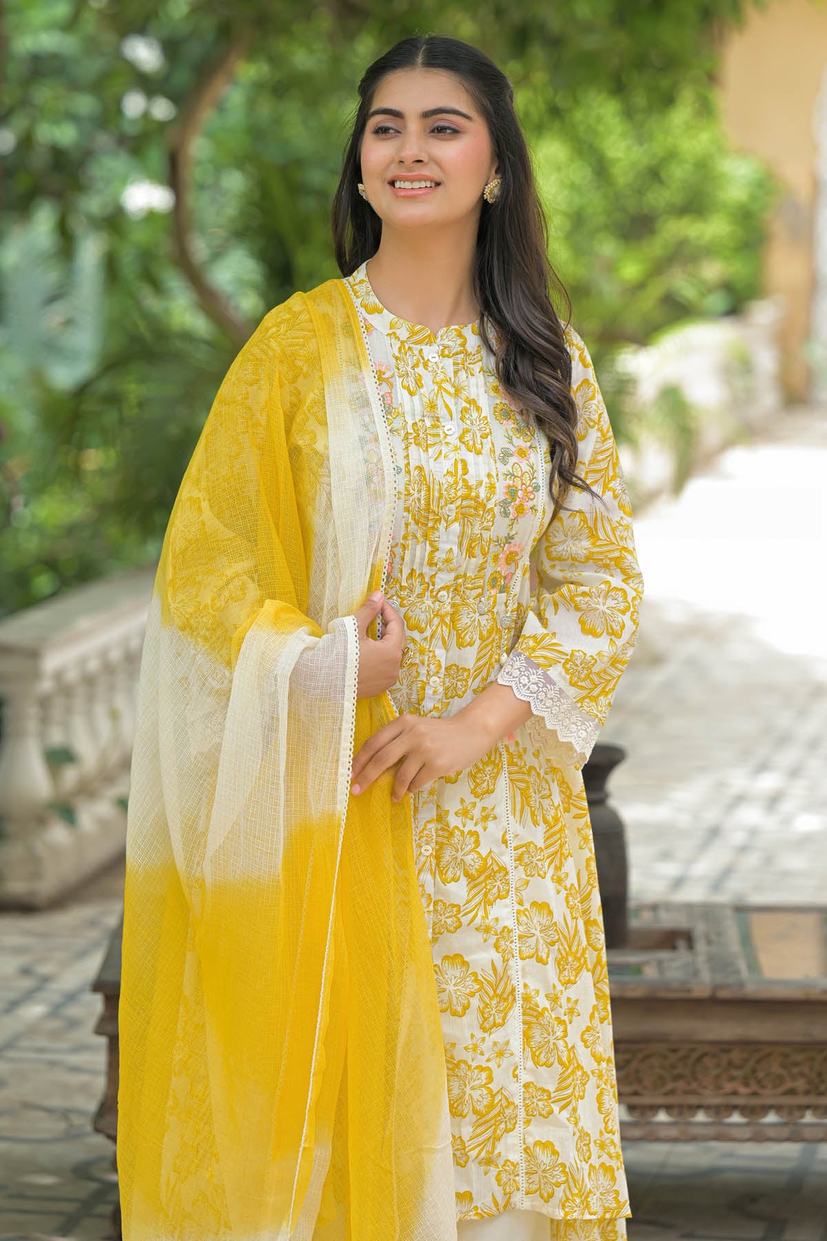 Woman wearing a yellow and white traditional outfit with a matching dupatta outdoors.