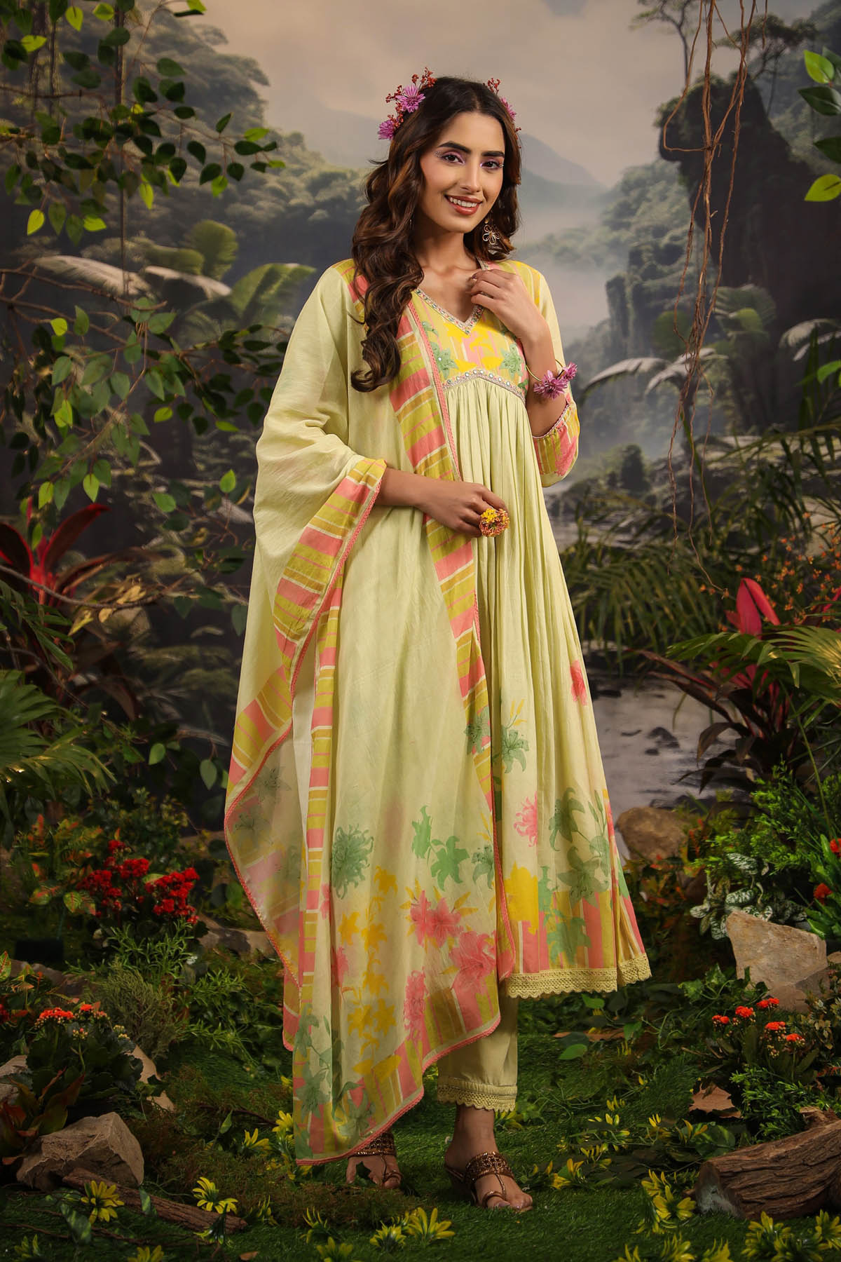 Woman in a light green traditional outfit with floral patterns standing in a natural setting.