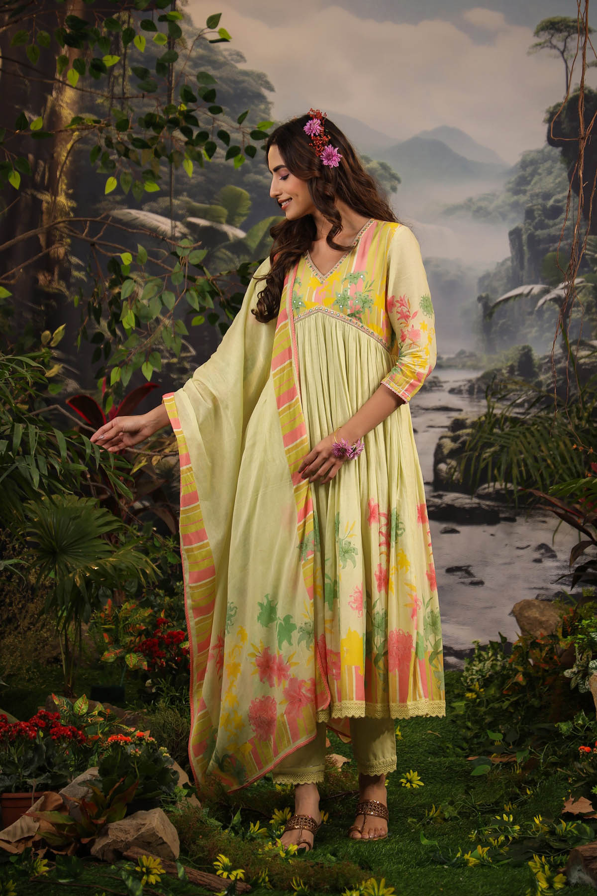 Woman in a floral dress standing in a nature-themed setting with mountains and water.