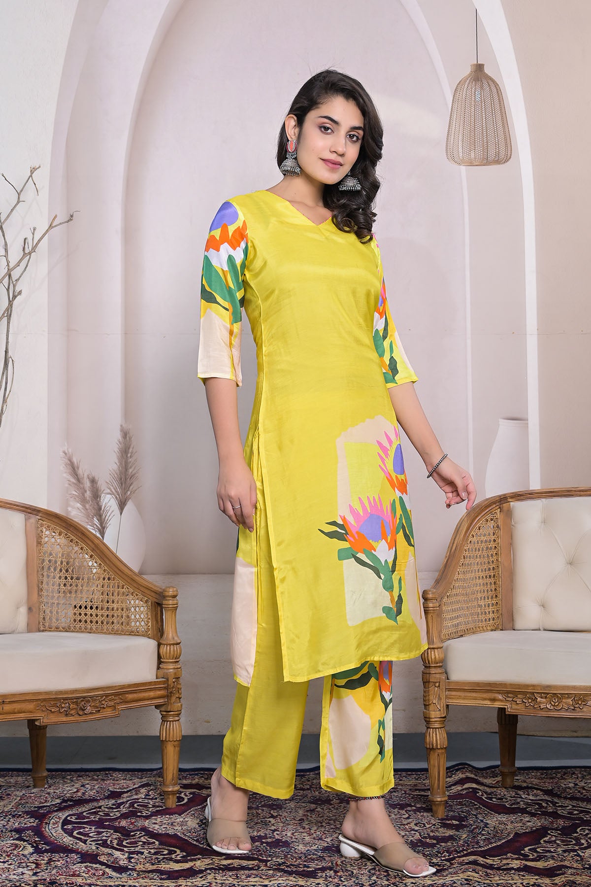 Woman wearing a yellow kurta with floral patterns in a room with wicker chairs and decorative items.