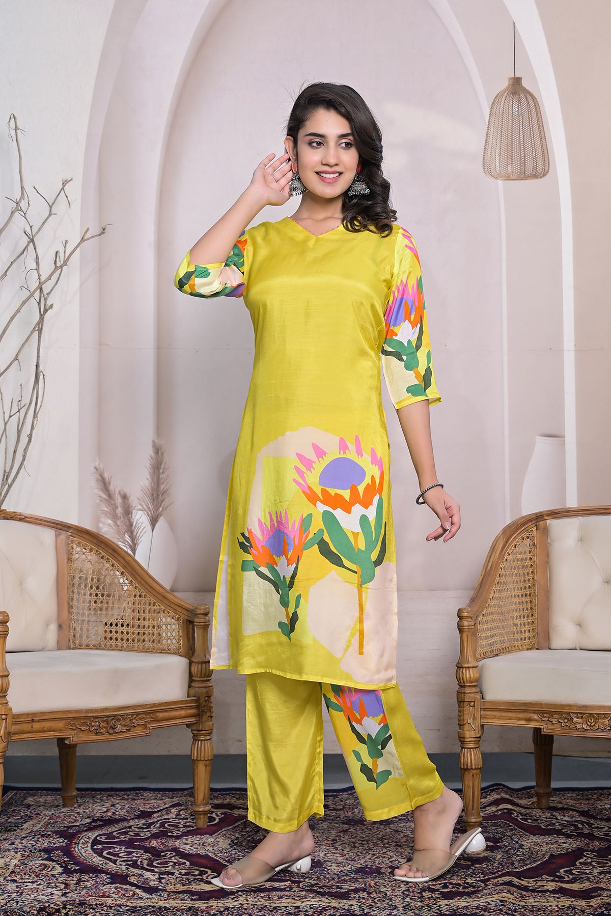 Woman wearing a yellow floral outfit in an elegant room with chairs and decor.