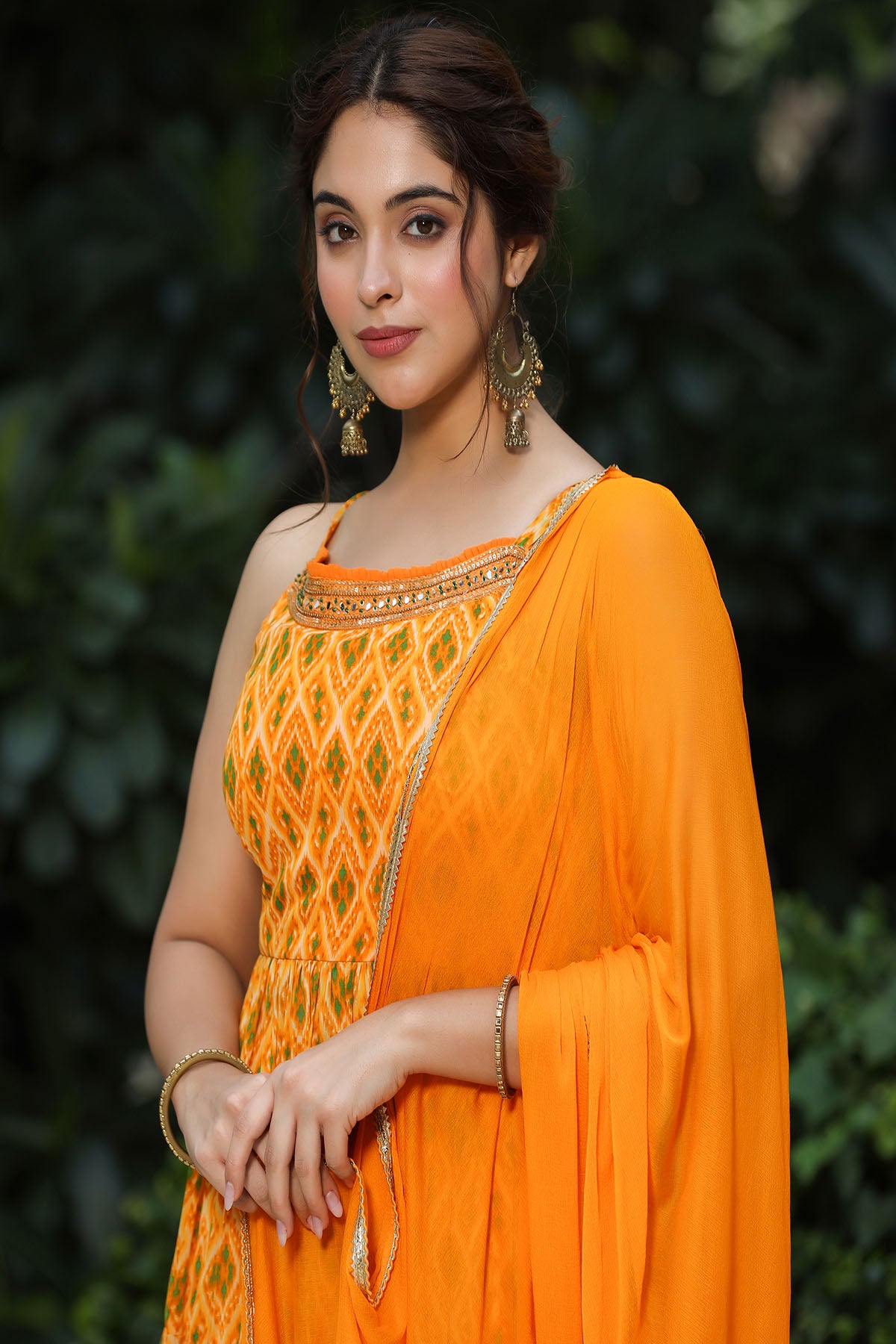 Woman wearing an orange traditional outfit with a patterned top against a blurred green background