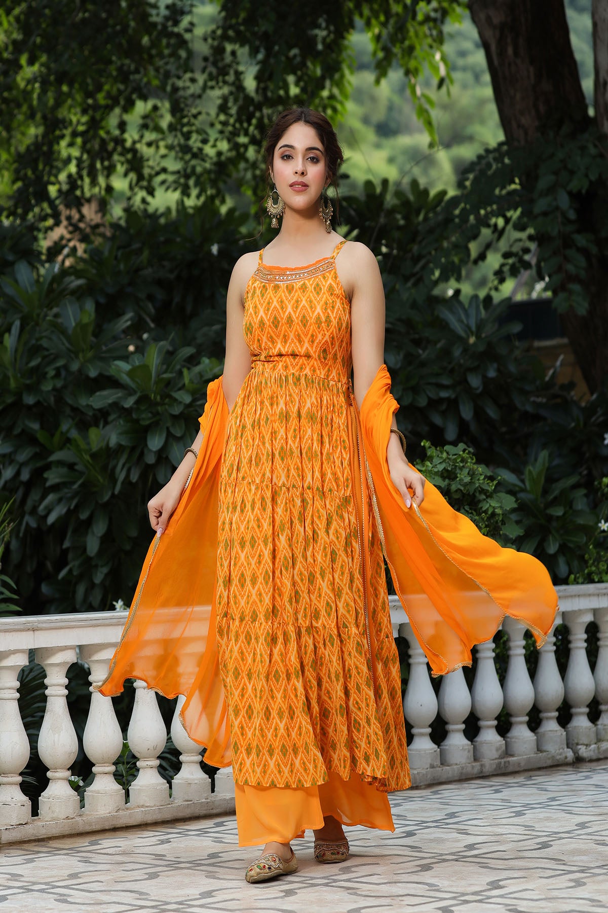 Woman wearing an orange traditional outfit with a patterned design, standing outdoors.