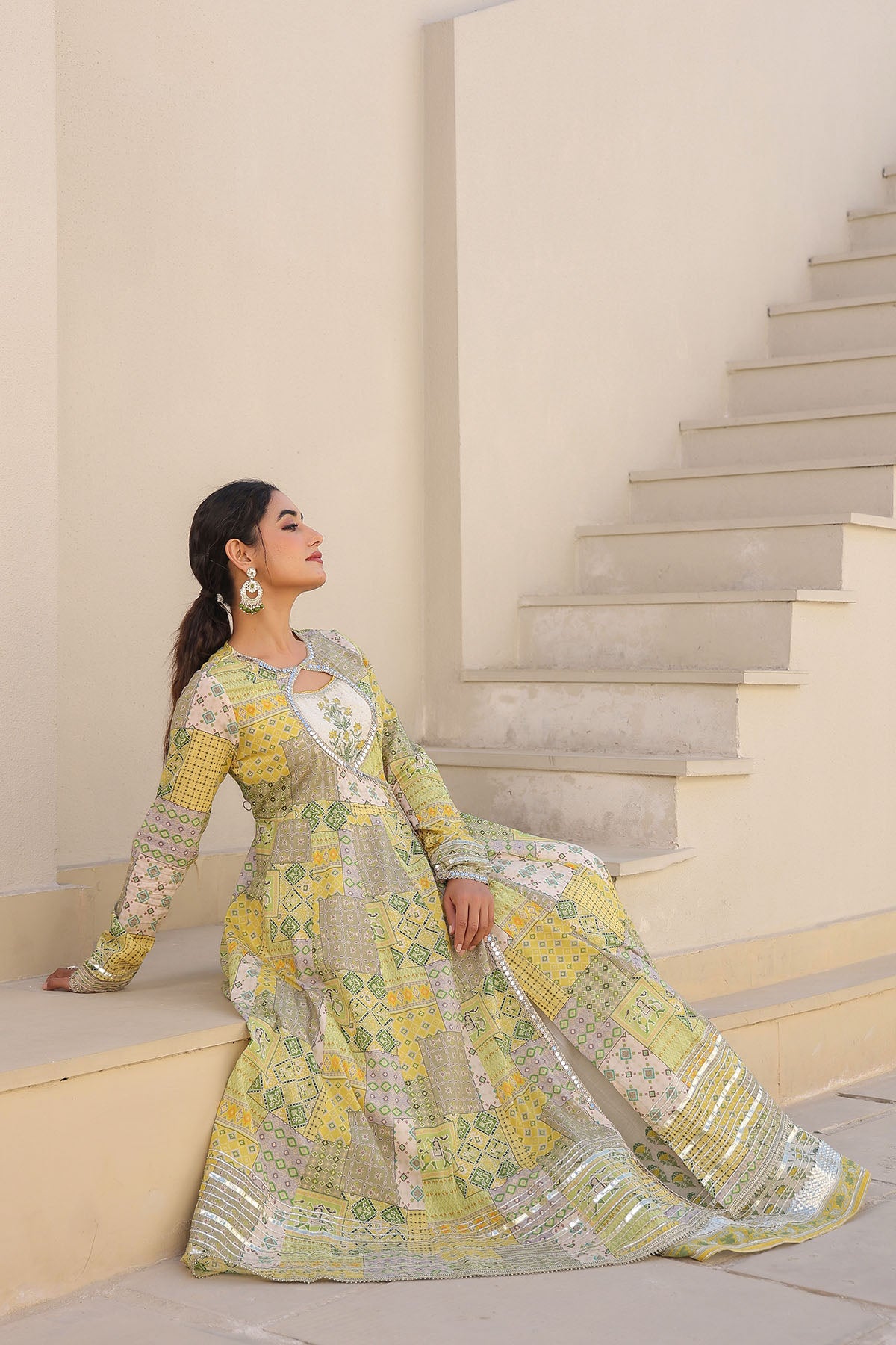 Woman in a yellow and green patterned dress standing on a staircase.