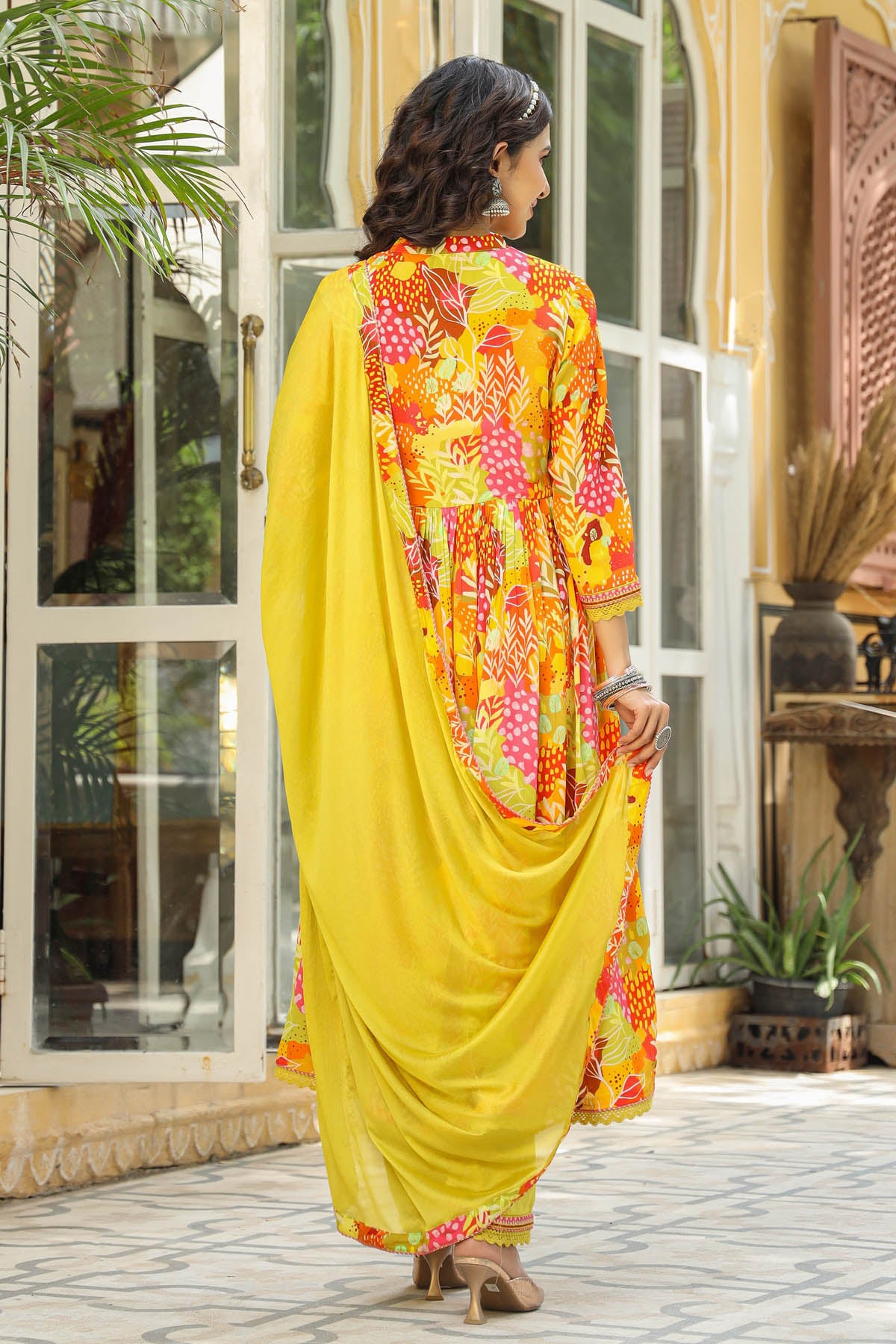 Woman in a bright yellow and multicolored traditional outfit standing in an outdoor setting.