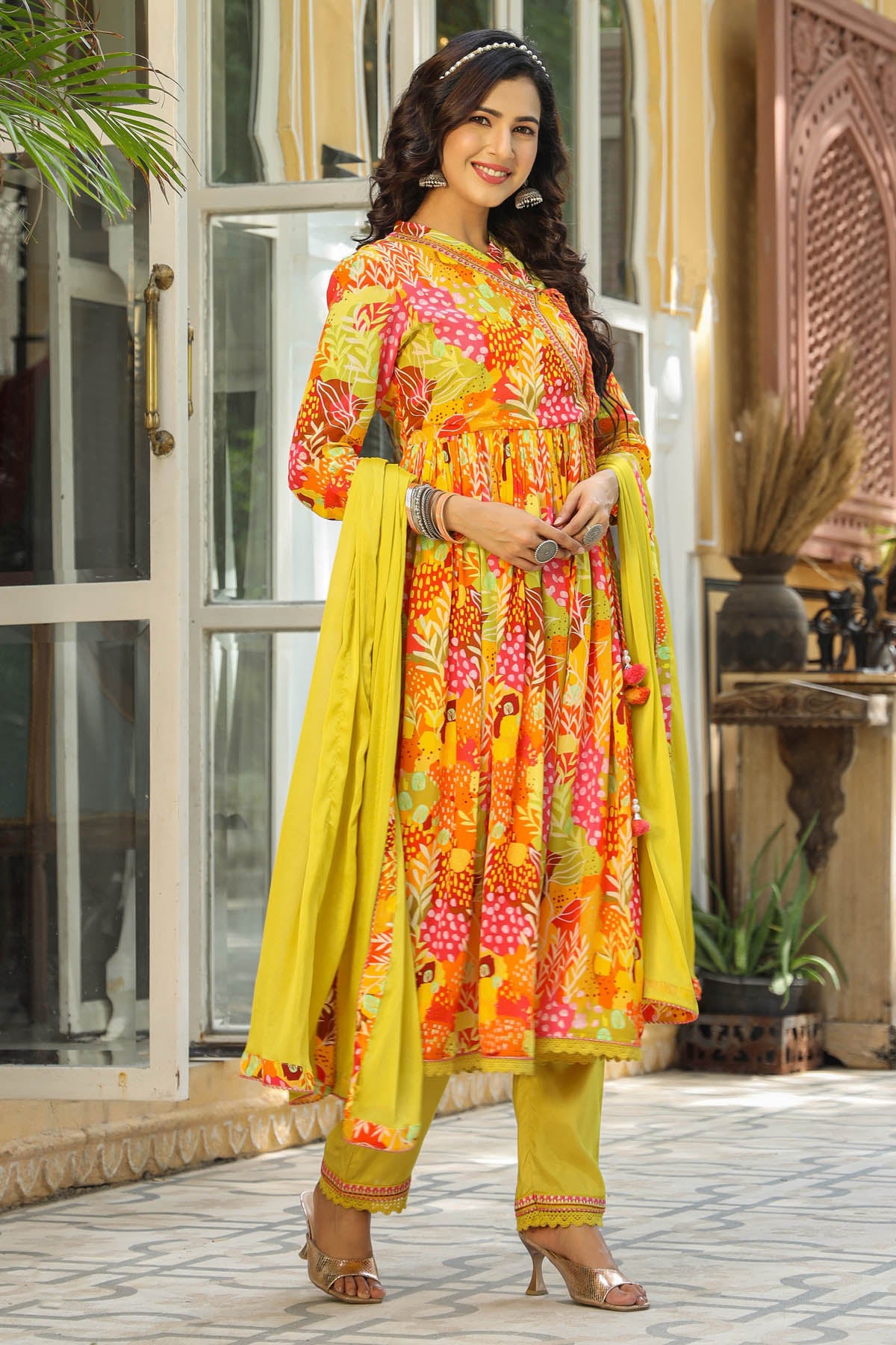 Woman in a colorful traditional outfit standing in front of a decorative entrance.