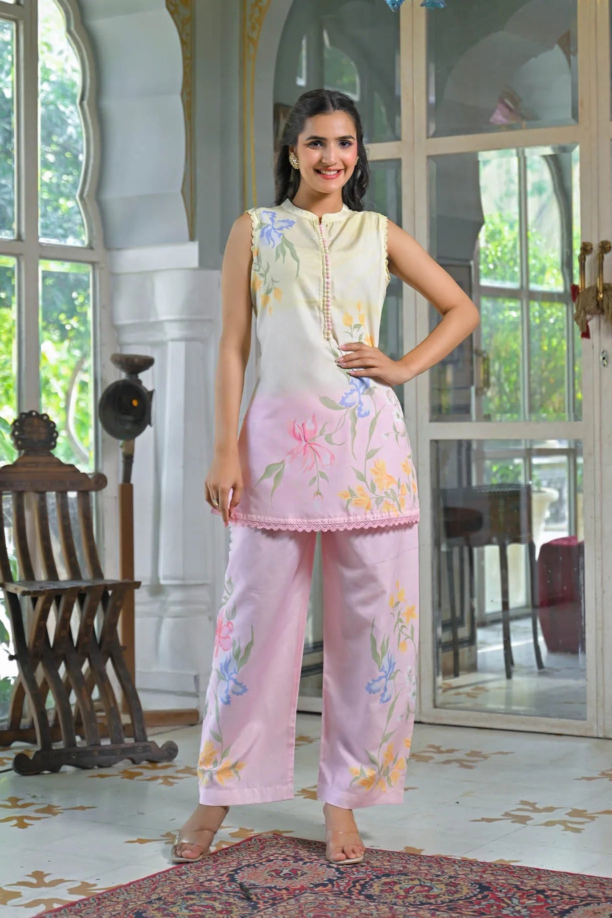 Woman wearing a floral dress and pants in a decorated room with large windows.