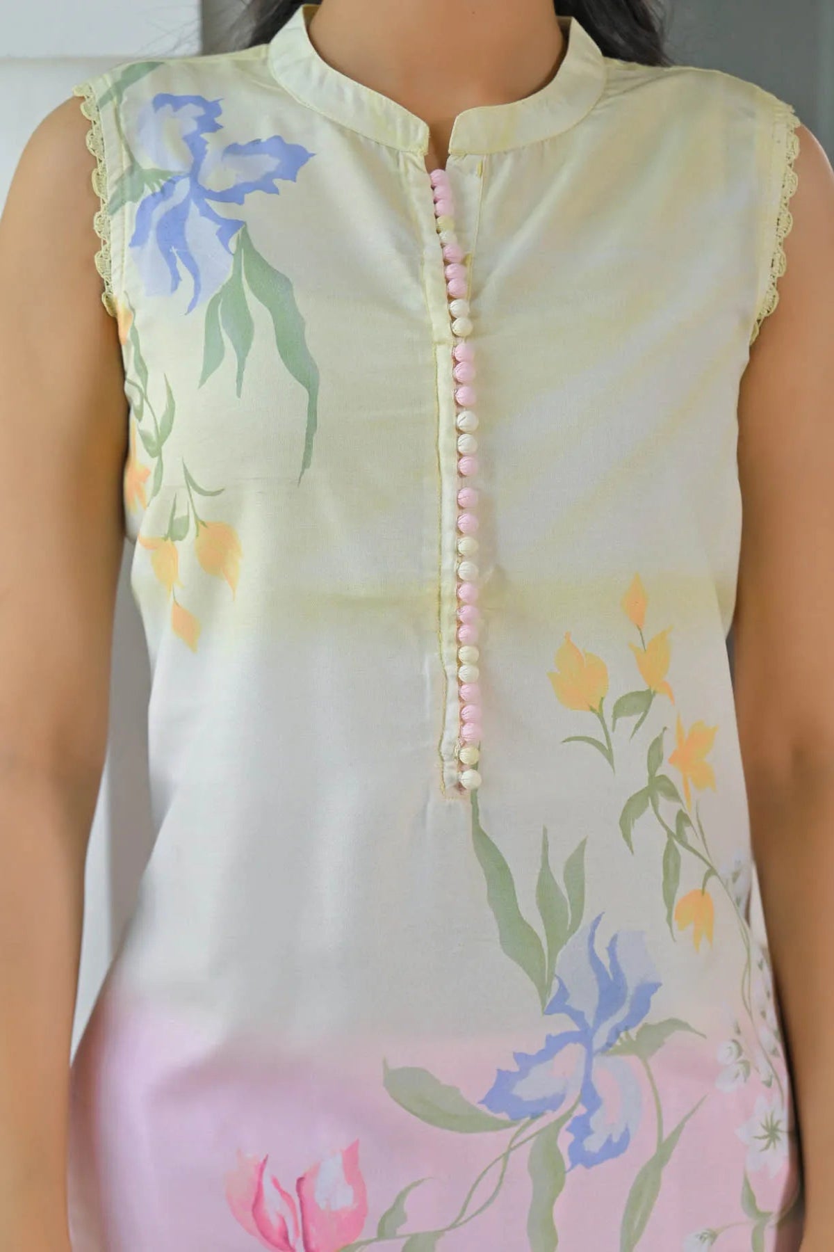 Light-colored sleeveless top with floral patterns and a decorative button detail.