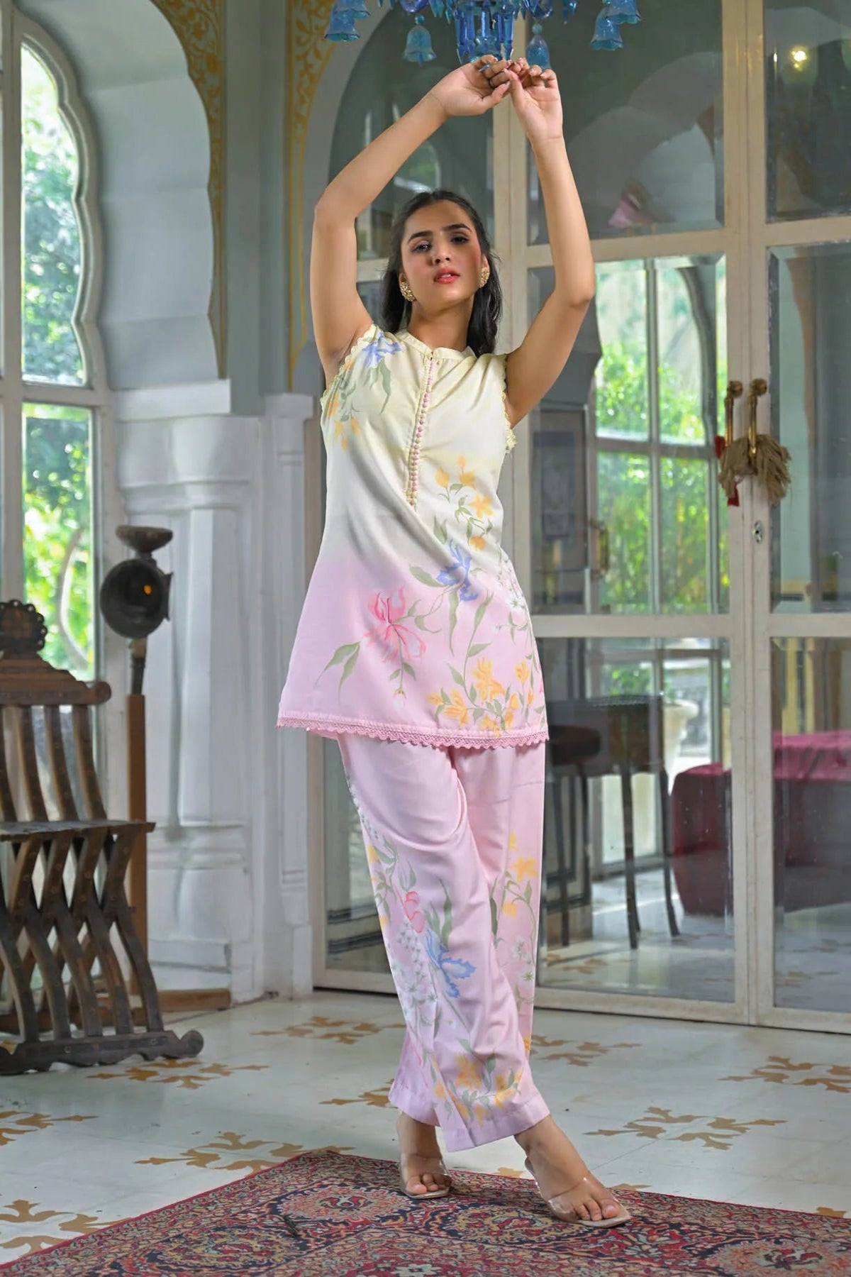Woman in a floral outfit standing in a room with large windows and decorative elements.