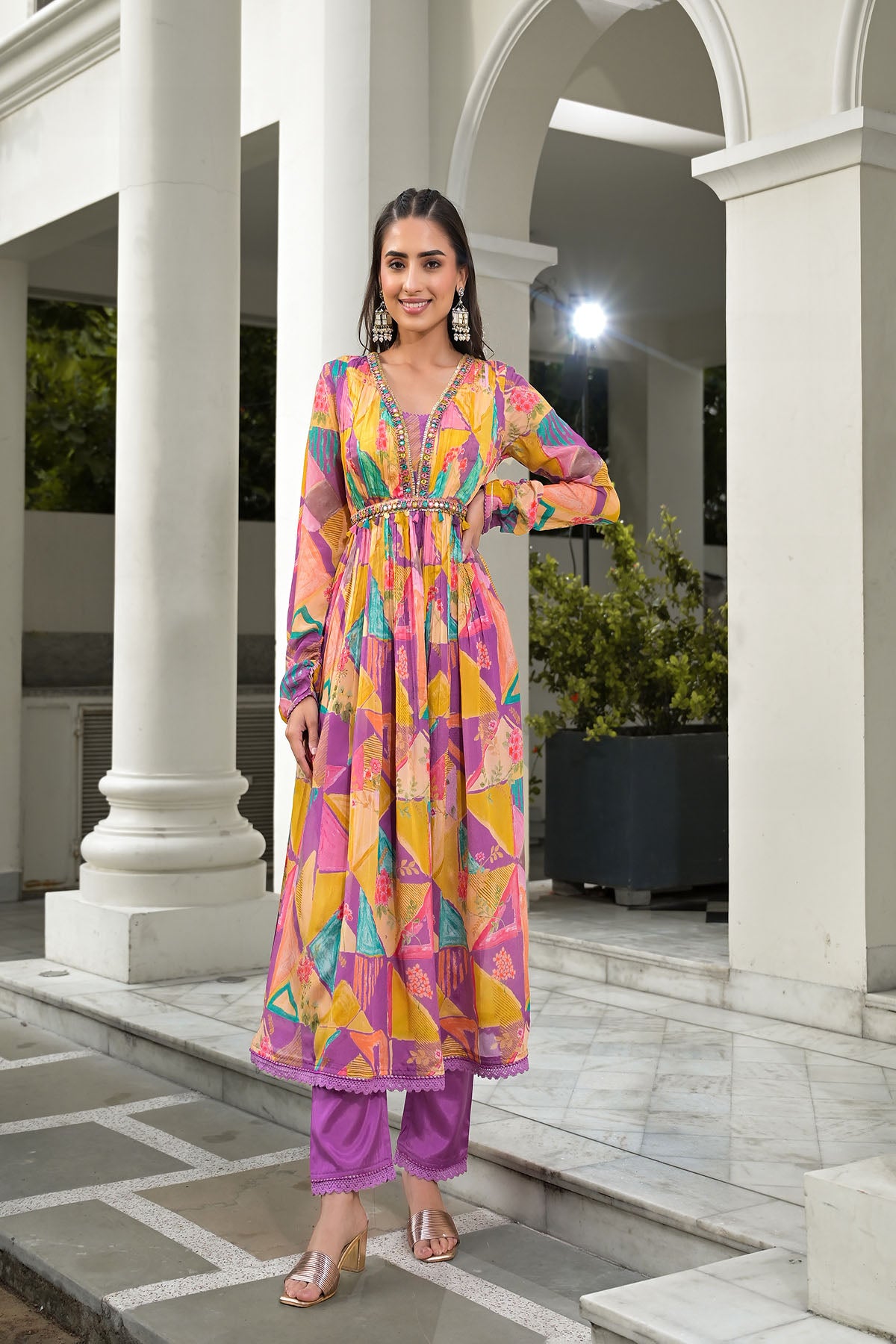 Woman in a colorful dress standing in an outdoor setting with columns and plants.