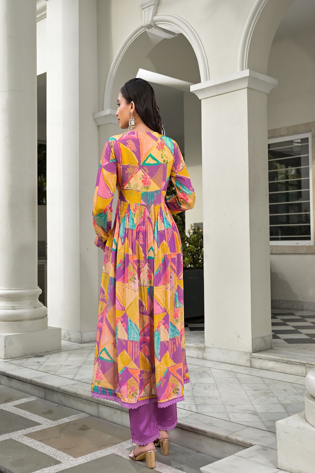 Woman in a colorful geometric-patterned dress standing in front of a white architectural structure.