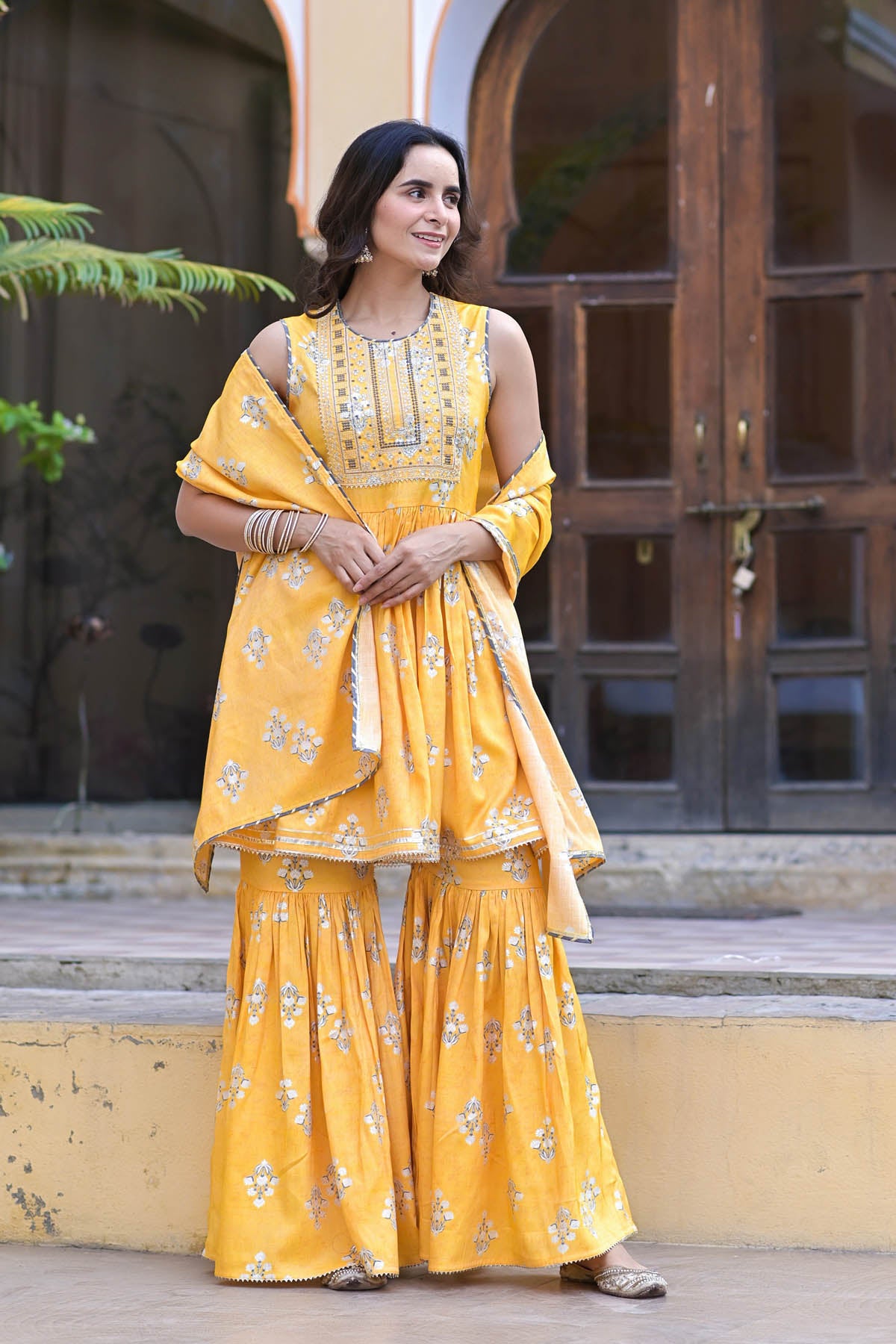 Woman in a yellow traditional outfit standing outdoors.