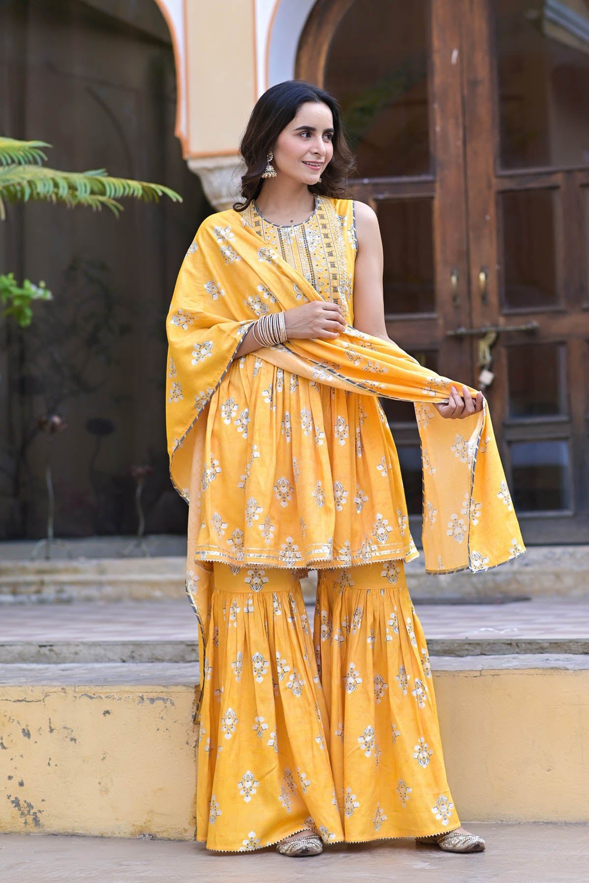 Woman in a yellow traditional outfit standing outdoors.