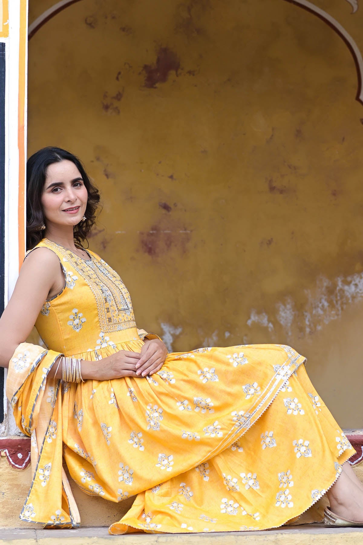 Woman in a yellow traditional outfit sitting against a yellow wall.