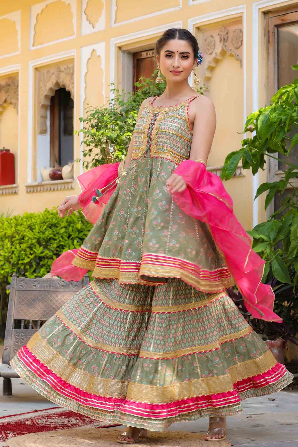 Woman in a traditional outfit with green and pink colors standing outdoors.