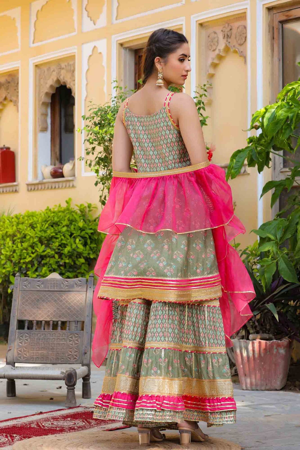 Woman in traditional green and pink outfit standing outdoors with decorative elements.